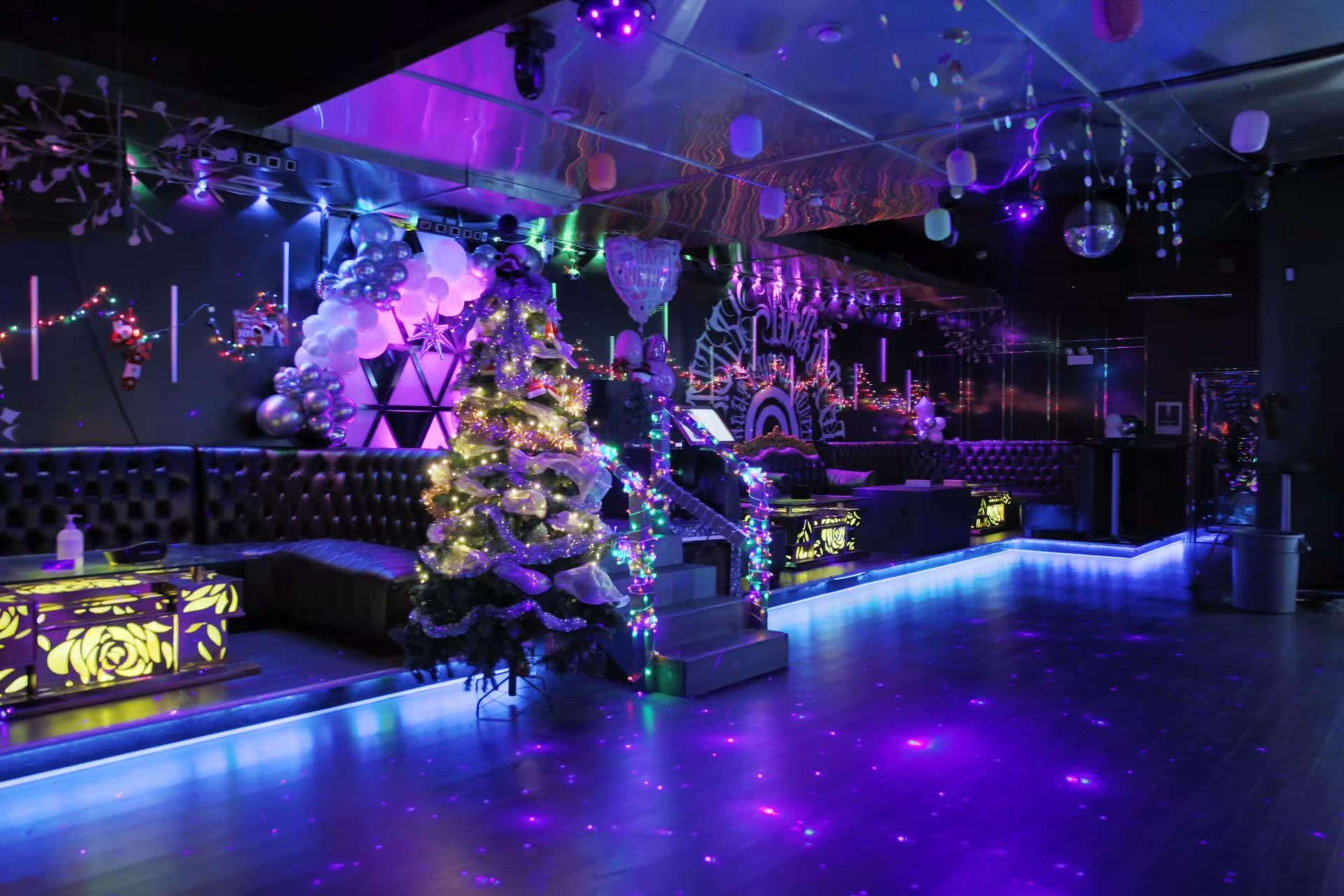 The image shows a dimly lit nightclub featuring vibrant purple and blue lighting, a decorated Christmas tree, and illuminated bar areas.