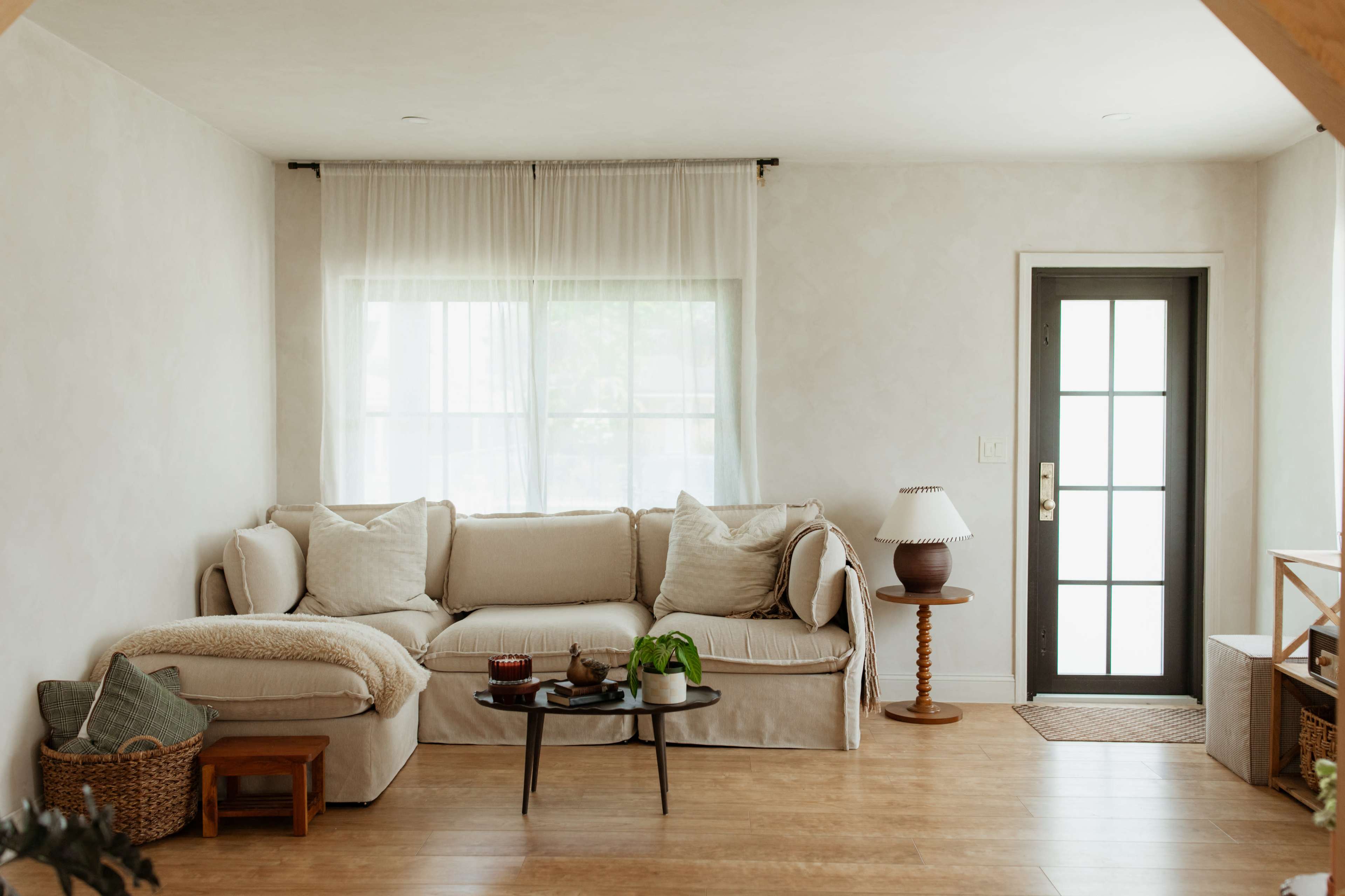The living room features a light-colored sofa with throw pillows, a small coffee table, a floor lamp, and a door with glass panels leading outside.