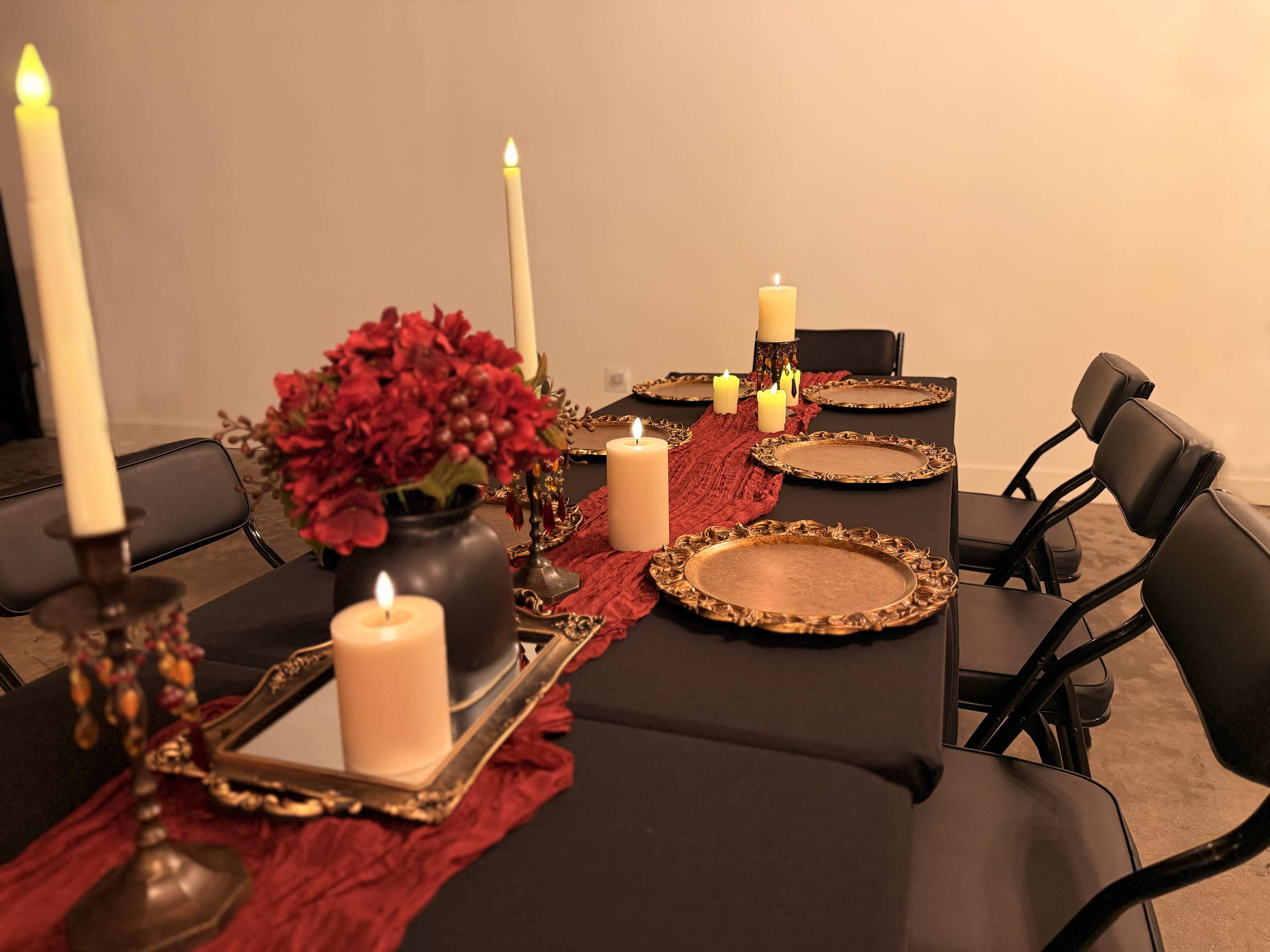 A long dining table is set with black cloth, decorative plates, candles, and a centerpiece of red flowers.