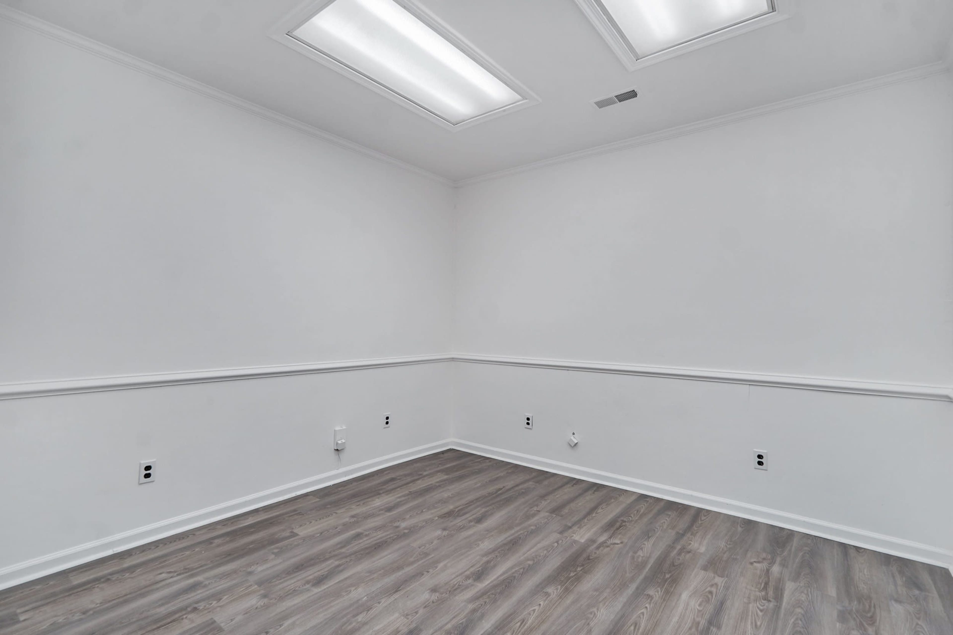 An empty room with white walls, a wooden floor, and two ceiling lights.