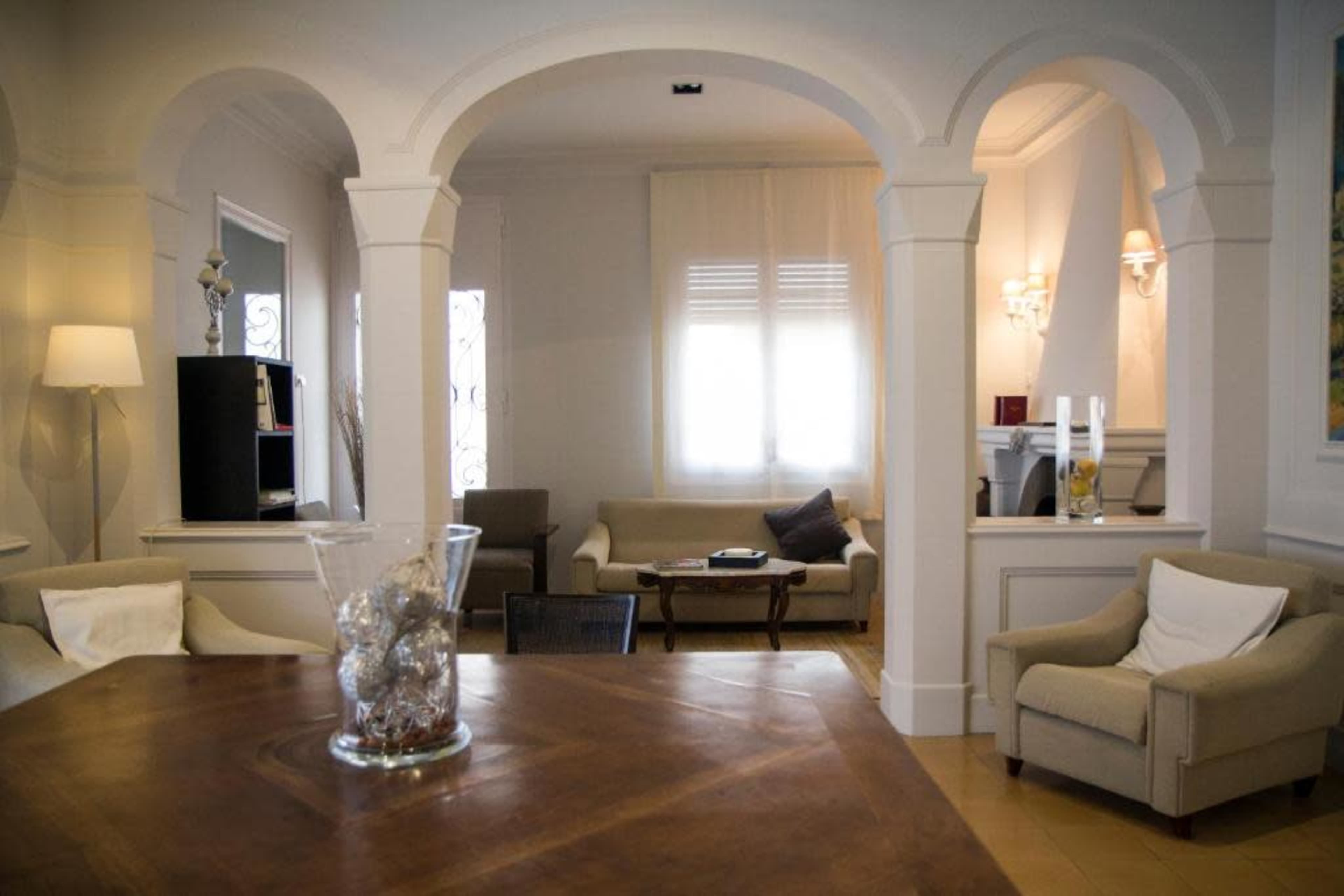 The image depicts a spacious, elegantly designed living area with archways, a wooden table in the foreground, and comfortable seating arrangements.