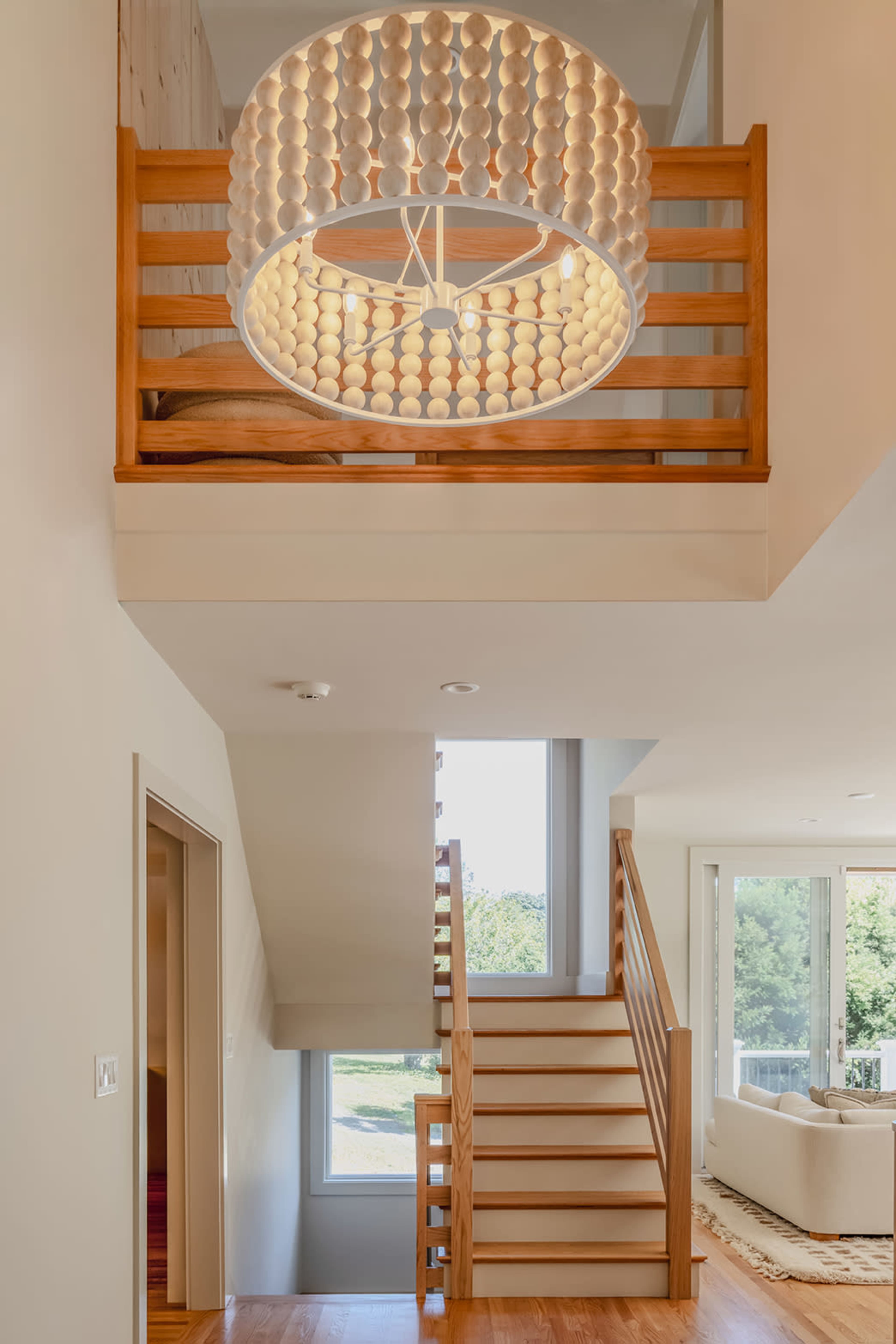 The image shows a modern interior with a staircase leading to an upper level, featuring a large round light fixture made of circular elements hanging from the ceiling.