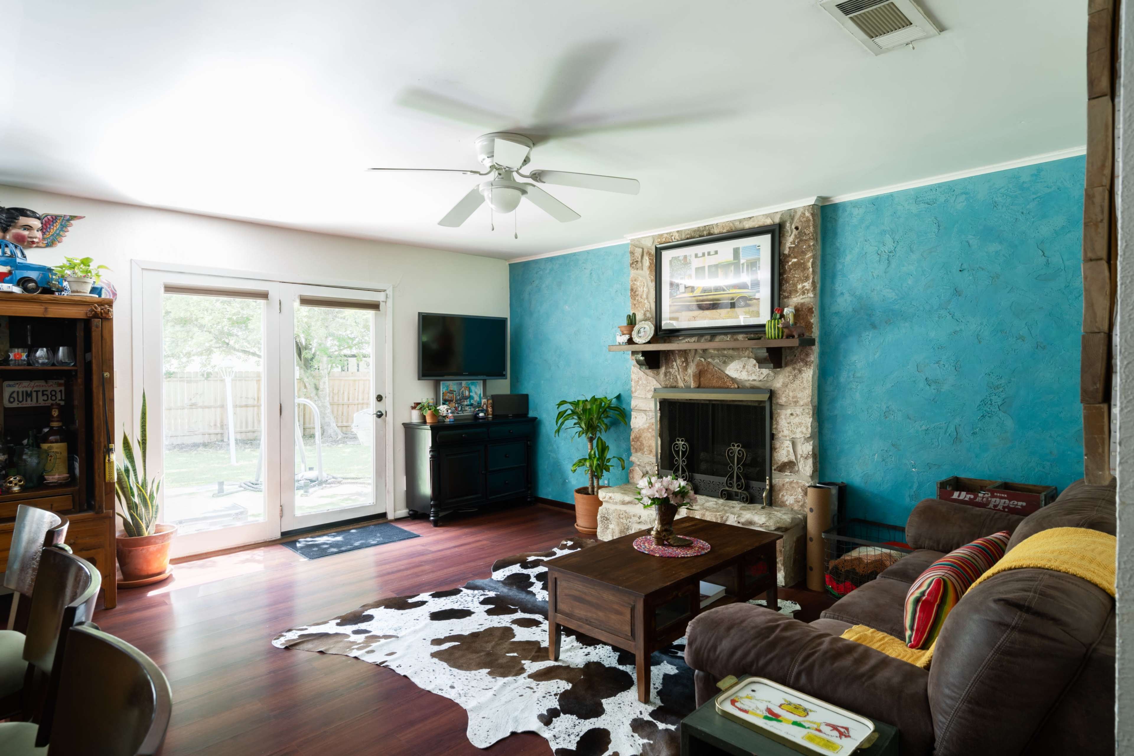 The living room features a stone fireplace, a wooden coffee table, and a wall painted blue, with a sliding glass door leading to an outdoor area.