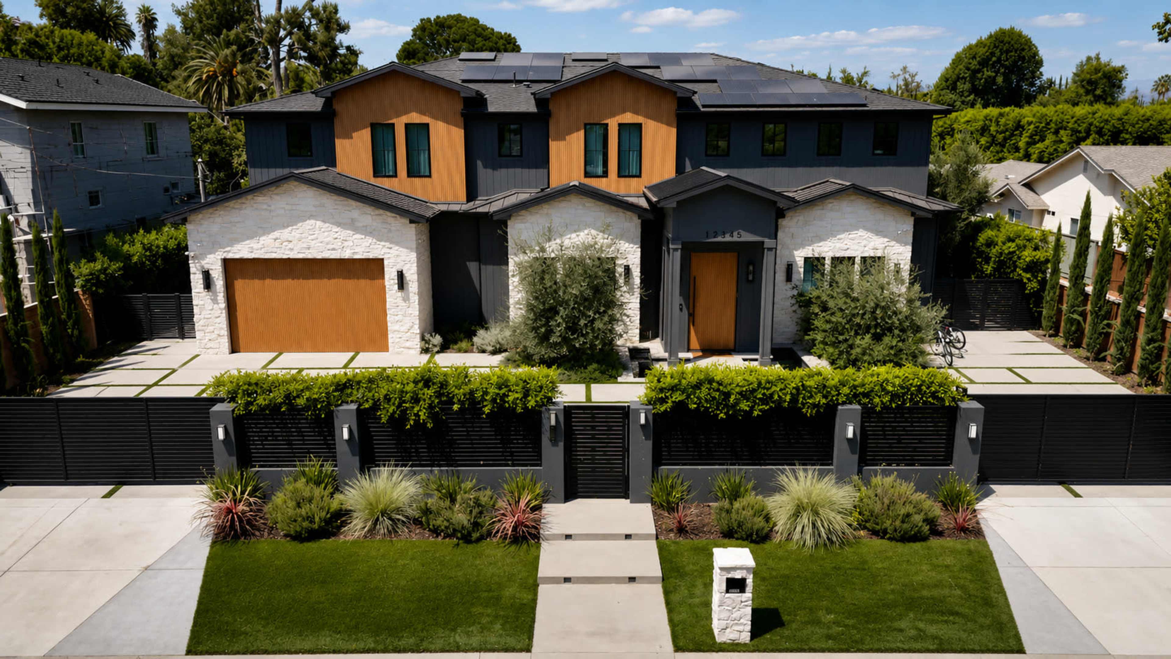 A modern two-story house with a combination of stone and wood accents is flanked by neatly trimmed hedges and a landscaped front yard.