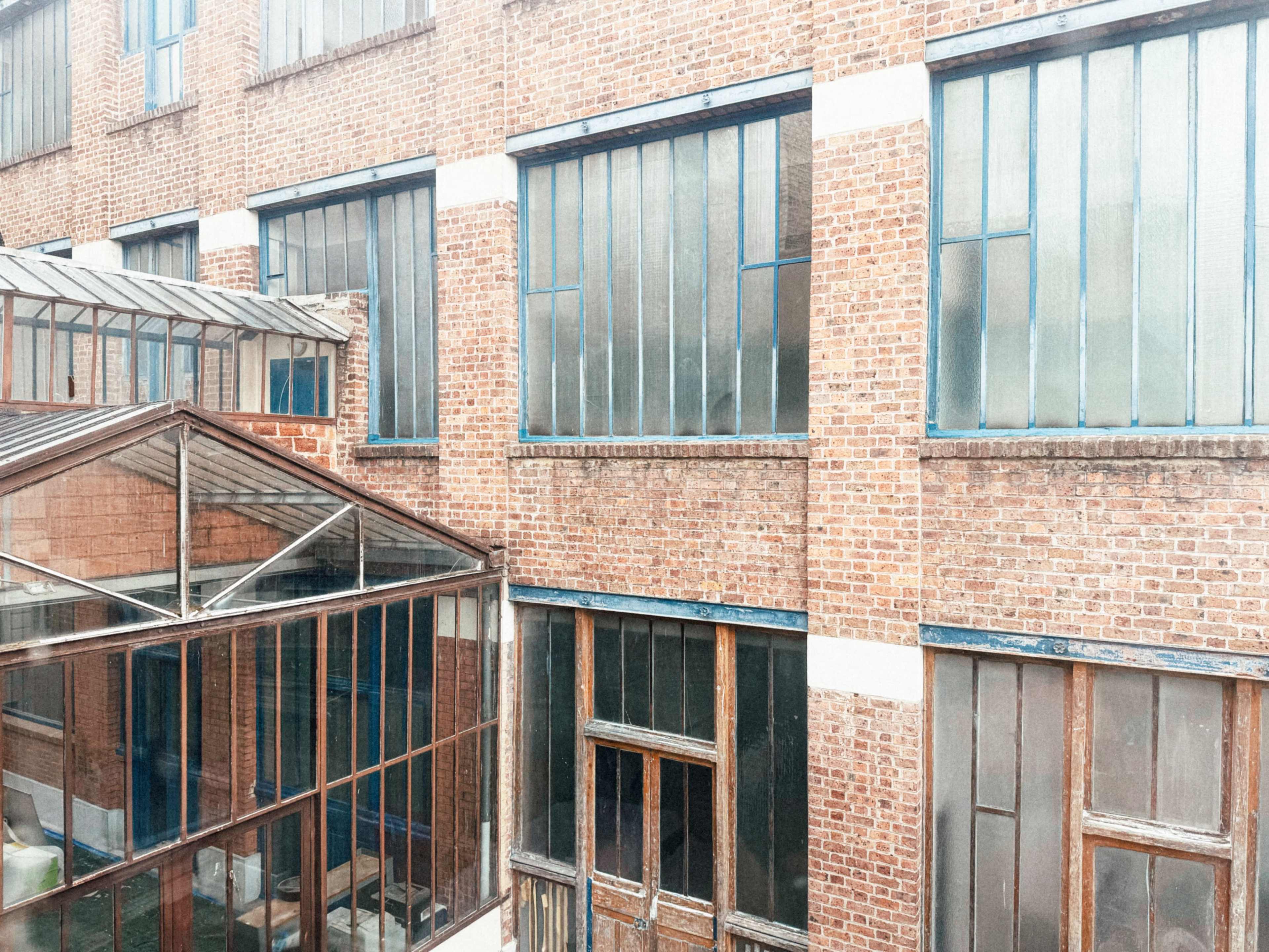 The image shows a brick building with large windows, featuring a glass-roofed structure in the foreground.