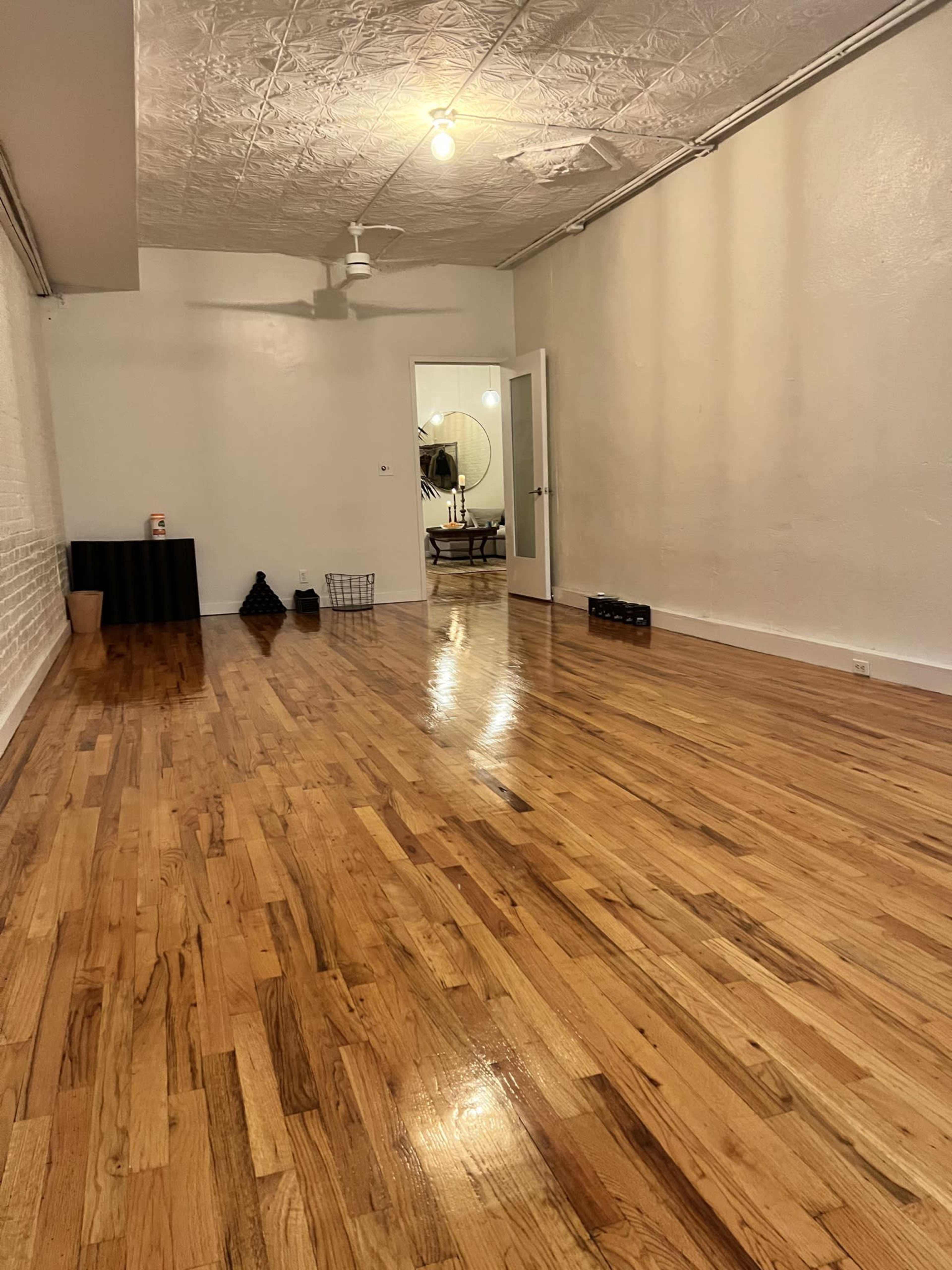 A spacious room with polished wooden floors, a white ceiling with decor, and minimal furnishings scattered throughout.