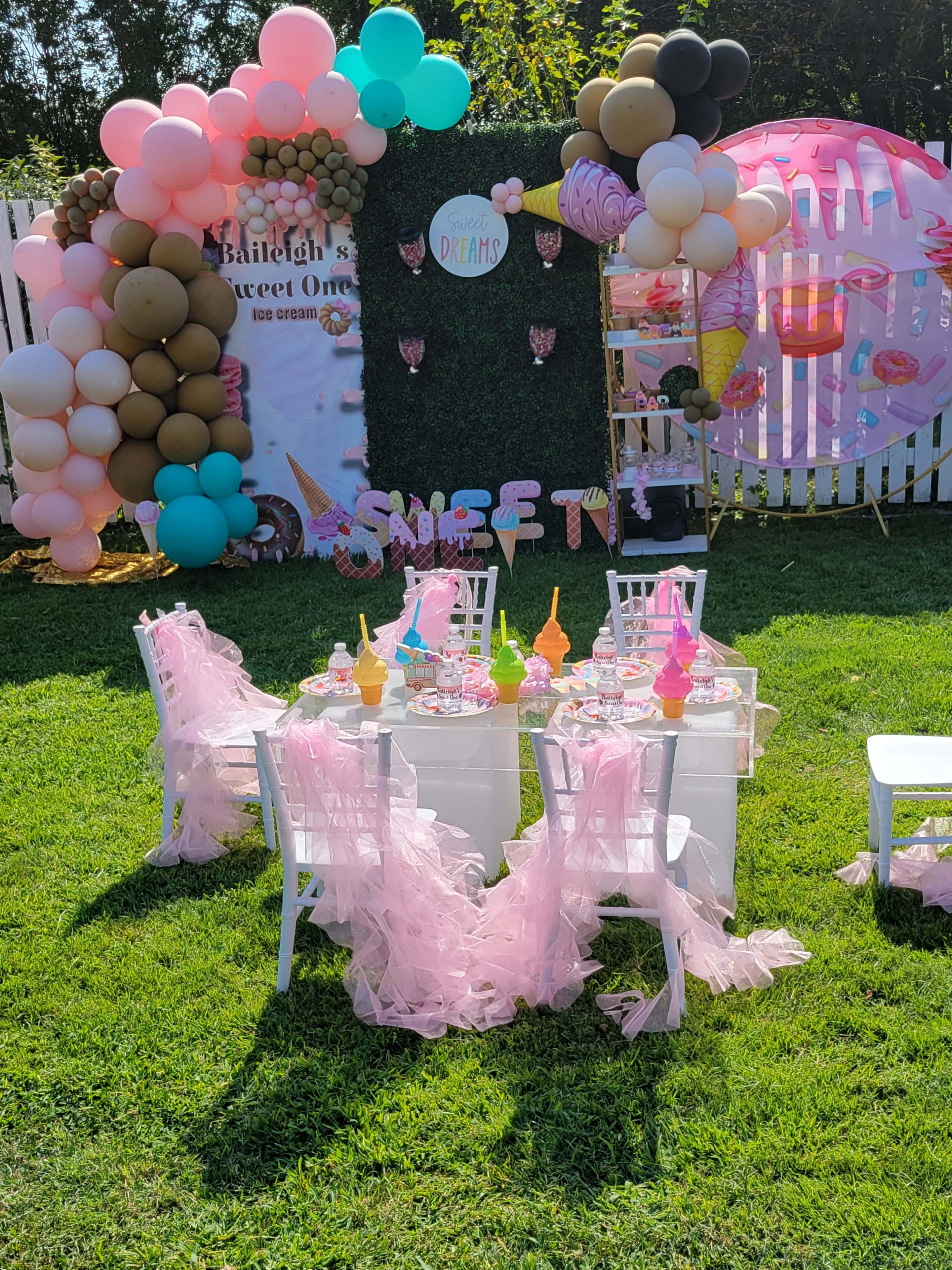 The image shows a decorated outdoor space for a party, featuring a table set with colorful ice cream-themed decorations, surrounded by balloons and a backdrop with the words "Sweet Dreams."