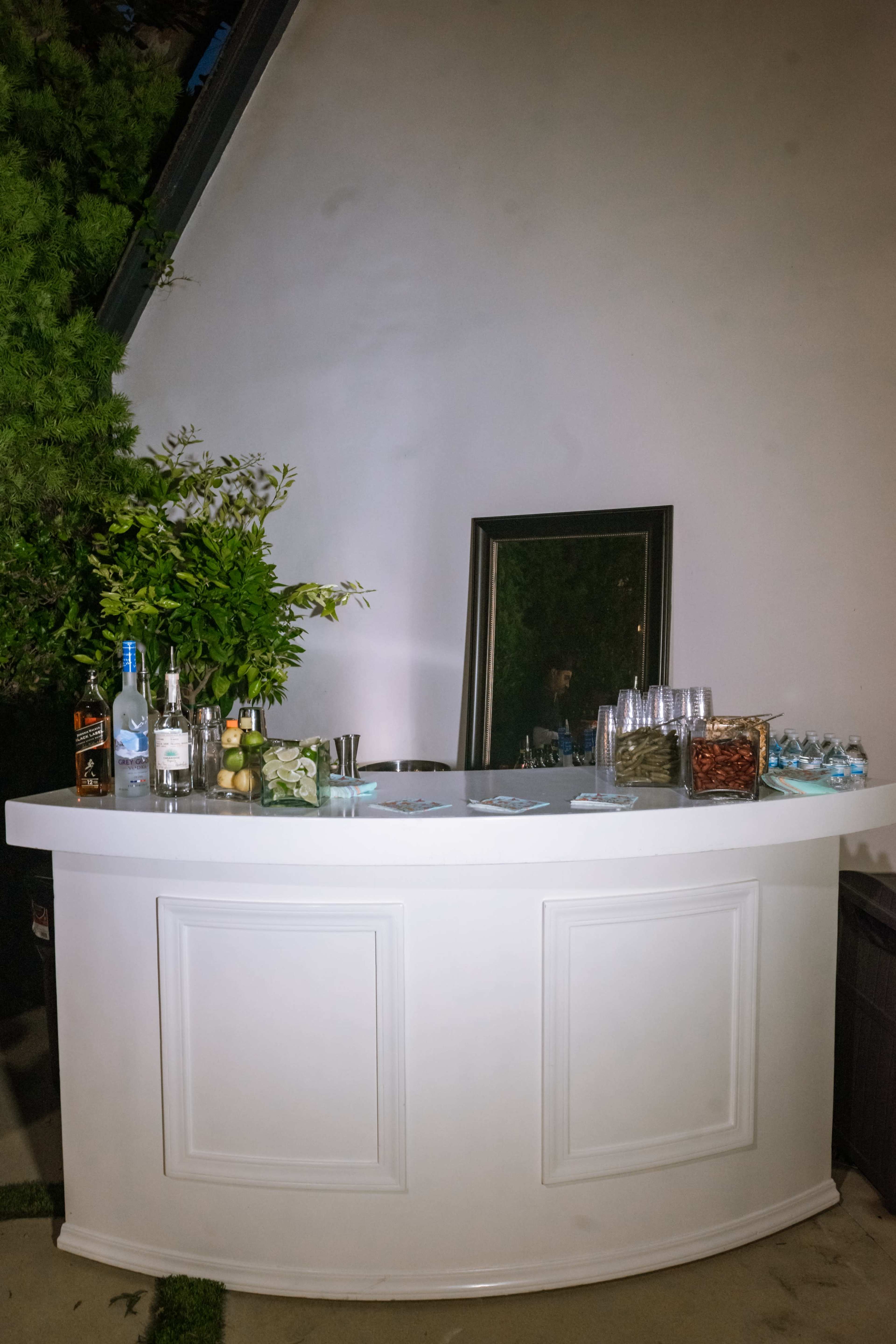 A white bar counter is set up against a wall, featuring various bottles, glasses, and a mirror.