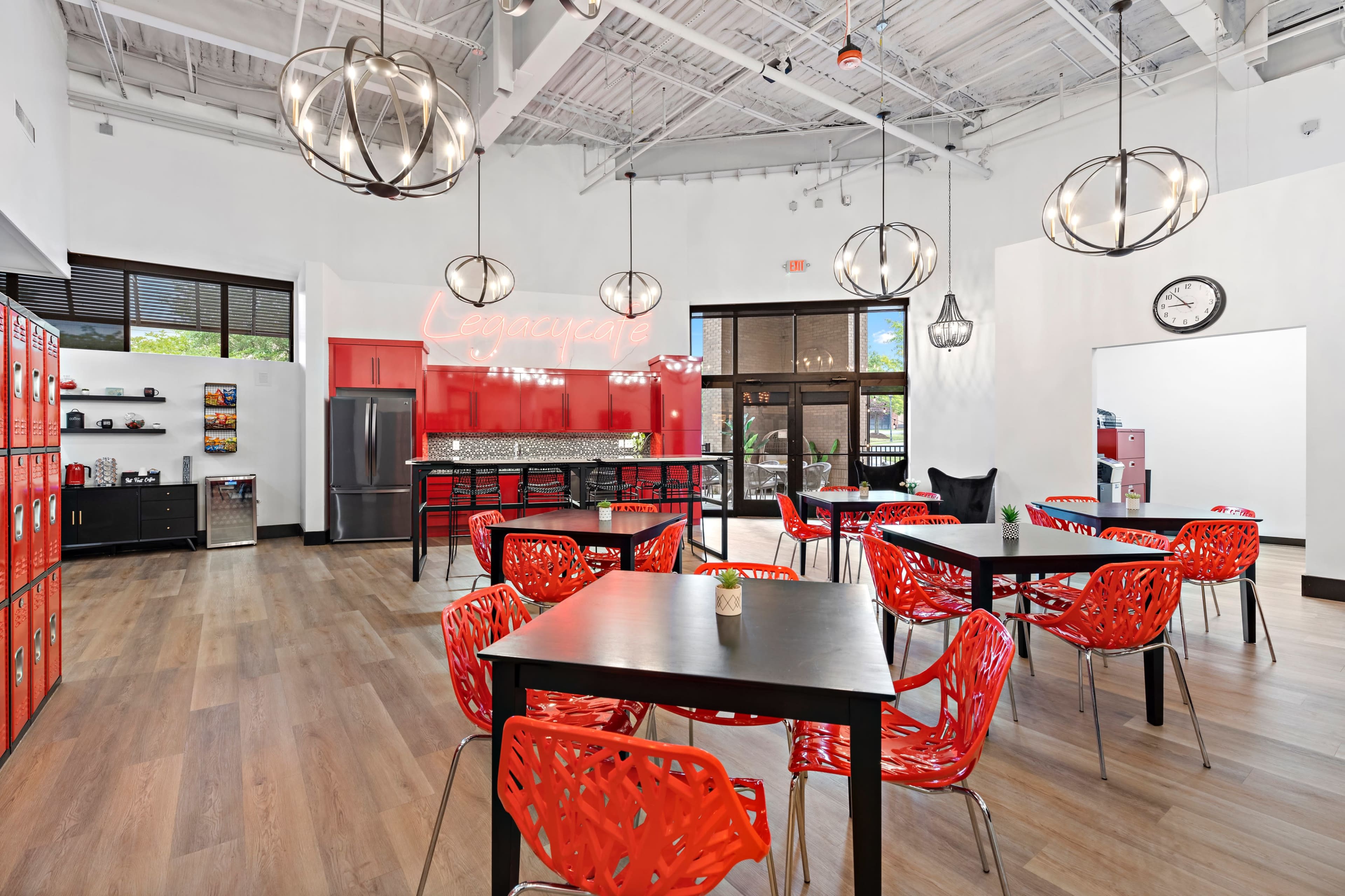 A modern communal kitchen and dining area featuring red chairs, a black kitchen counter, and large pendant lights.