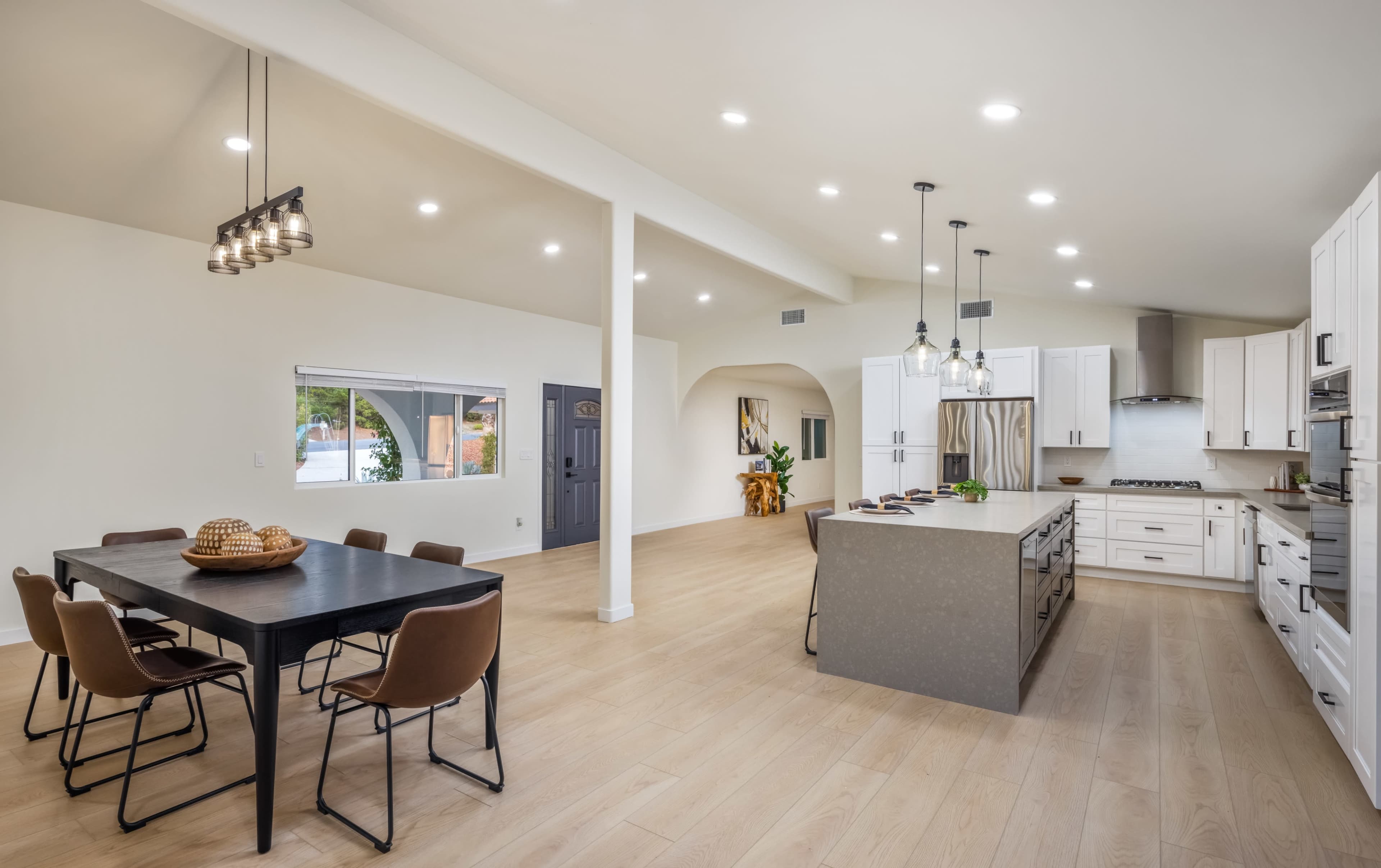A modern kitchen and dining area with a large island, a dining table with chairs, and bright overhead lighting.