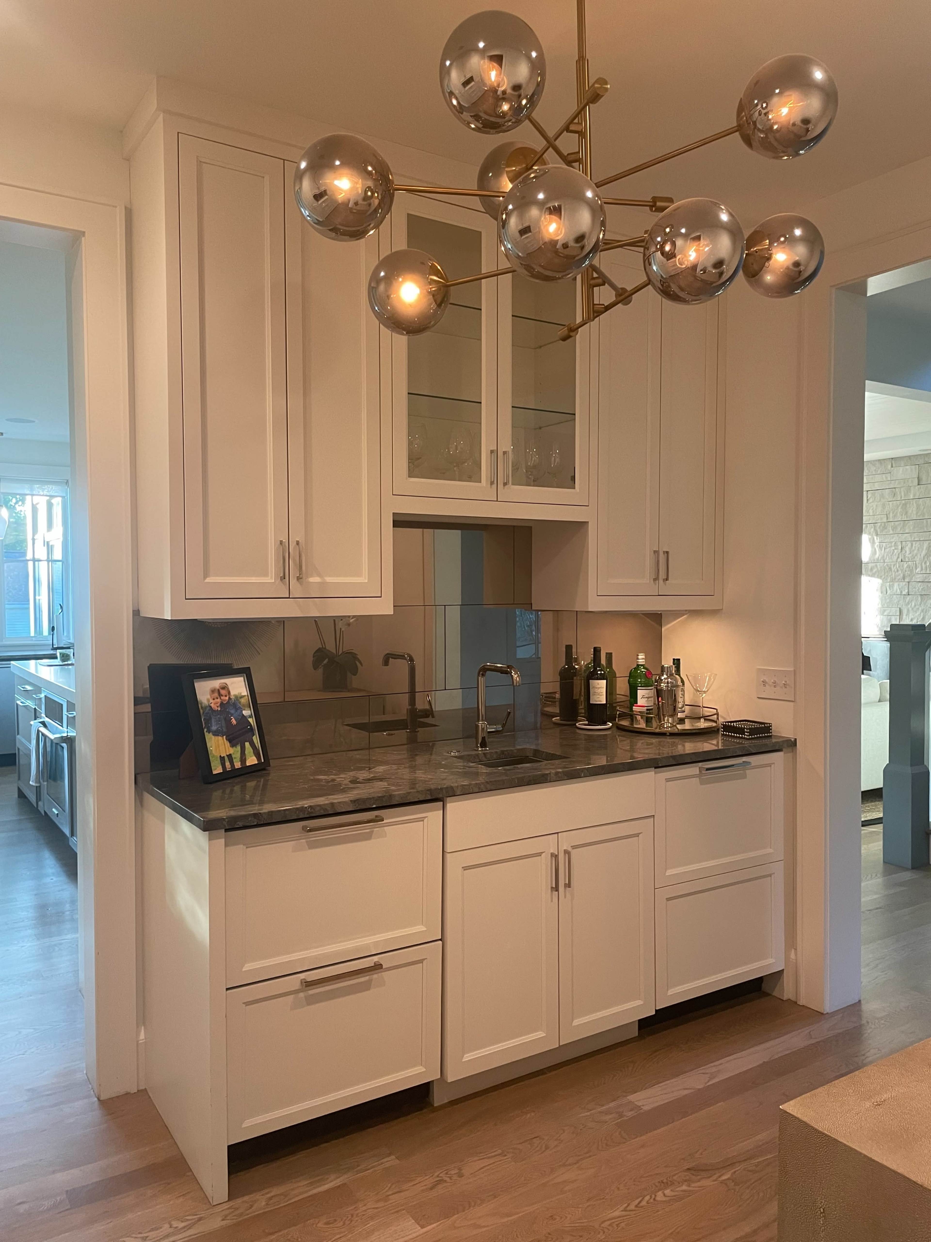 The image shows a modern kitchen with white cabinetry, a dark countertop, and a decorative light fixture with spherical bulbs.