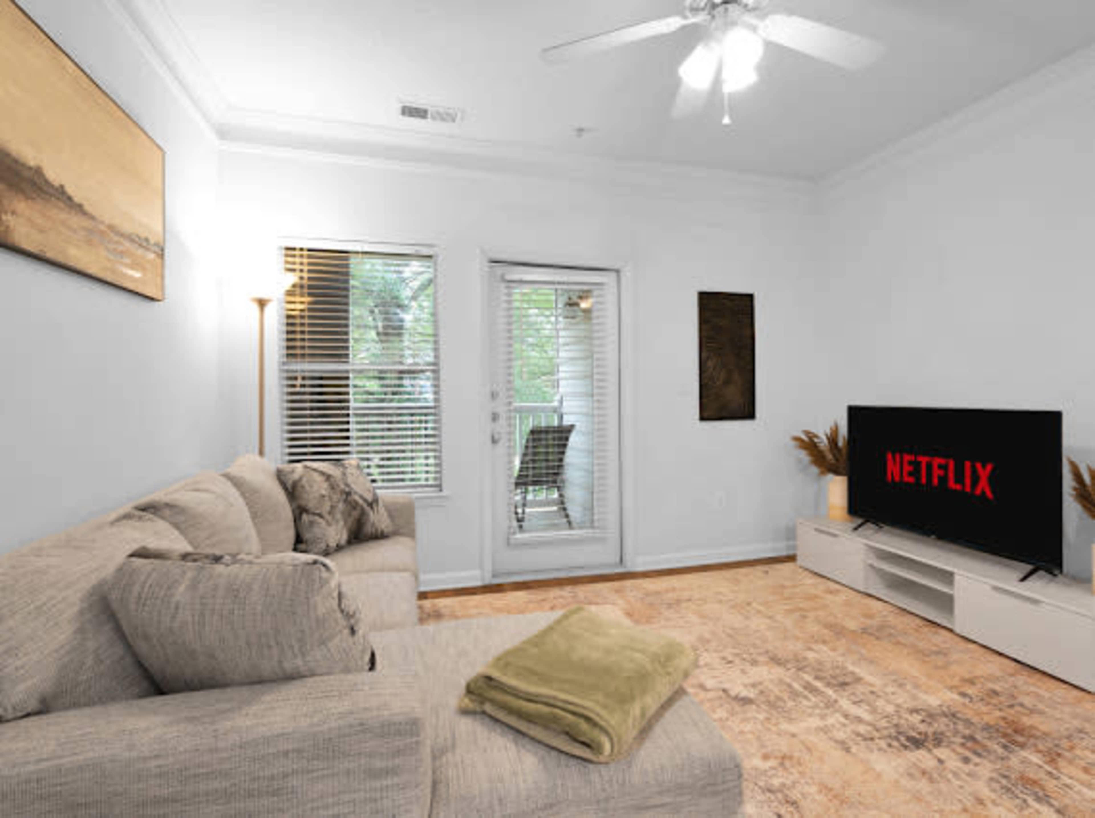 The living room features a sectional sofa, a TV with a Netflix display, and large windows overlooking a balcony.