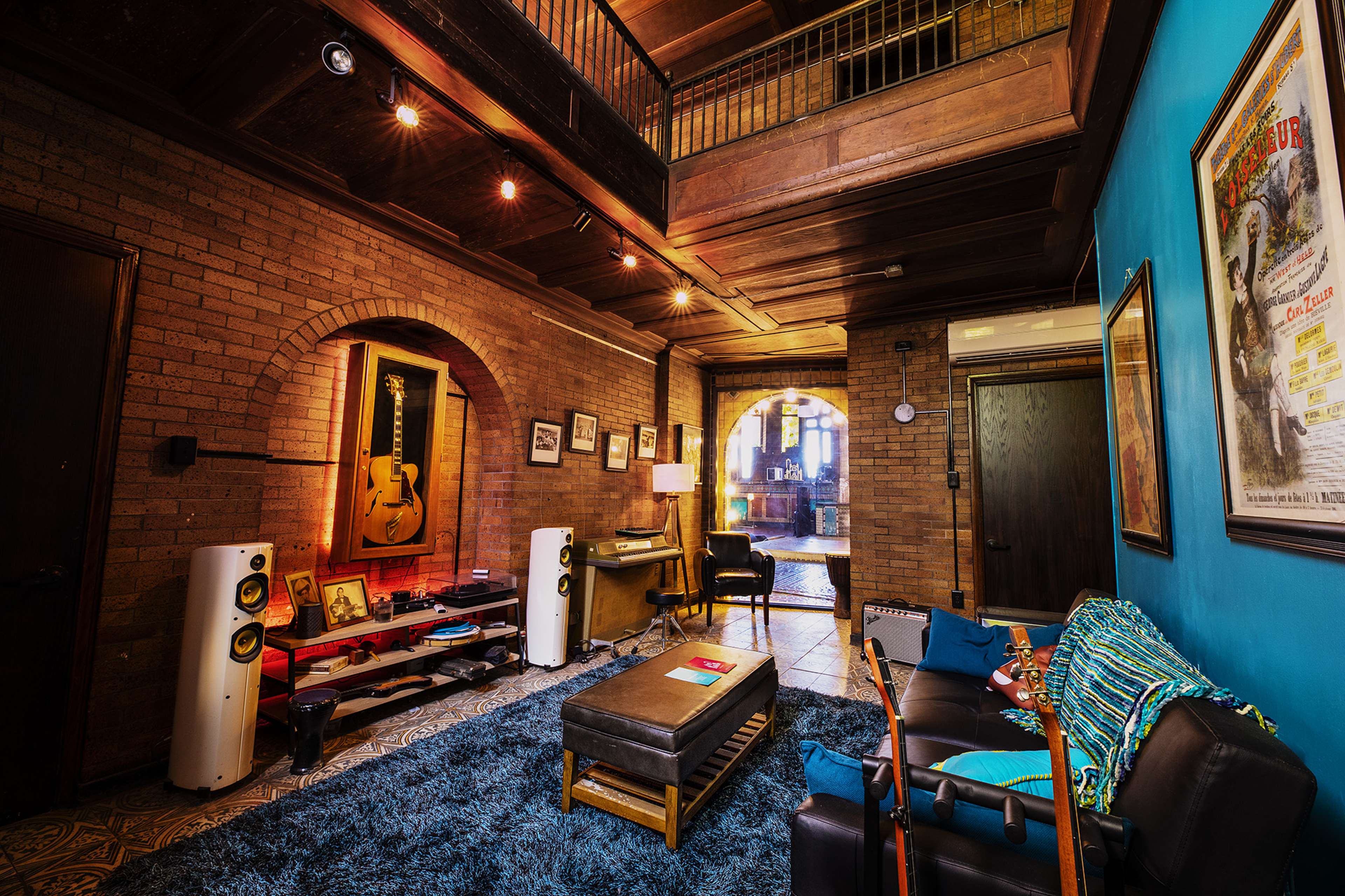 A spacious living room with exposed brick walls, wooden beams, and a blue accent wall, furnished with a couch, a coffee table, and audio equipment.