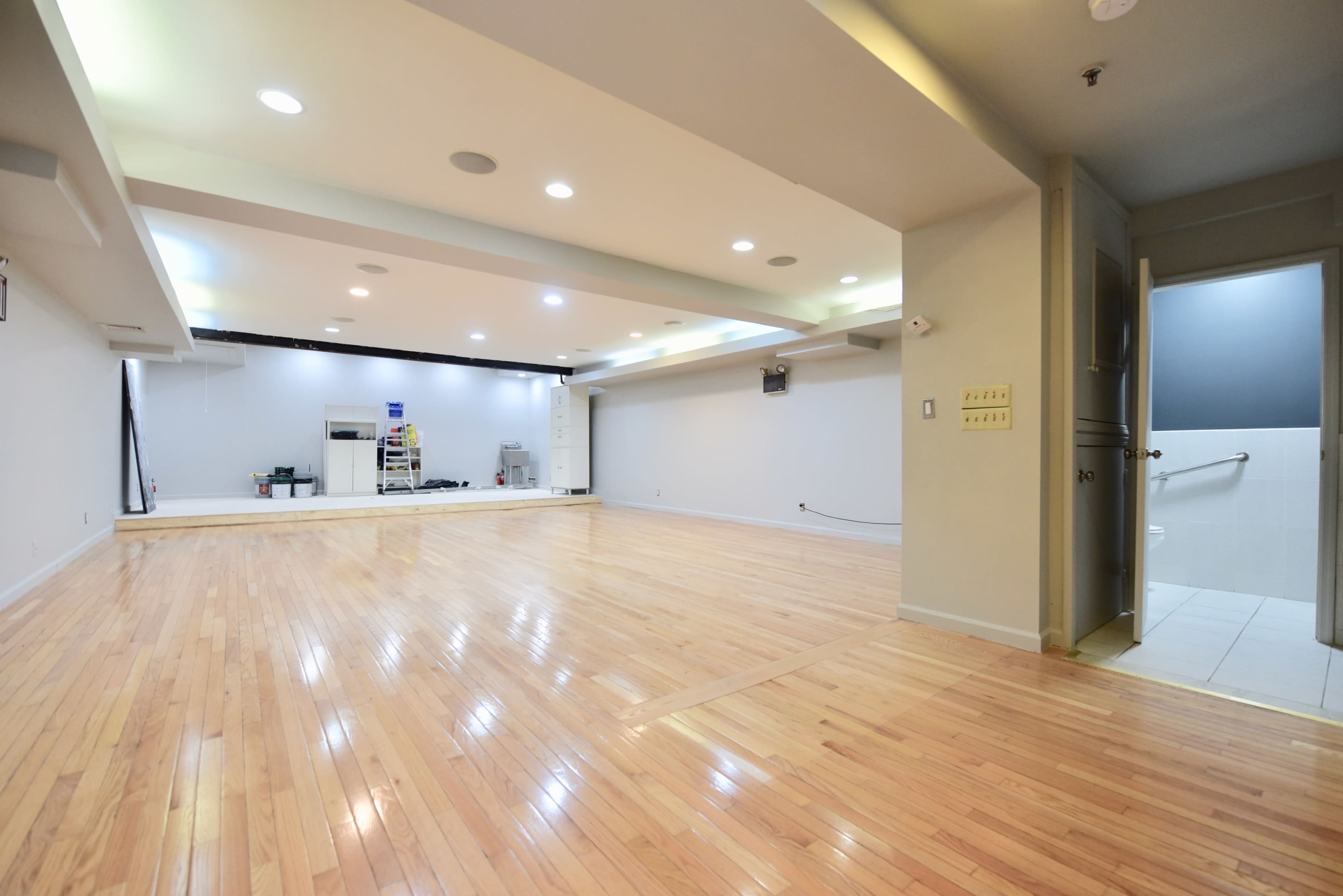 A spacious, well-lit room with polished wooden flooring and an adjacent bathroom entrance.