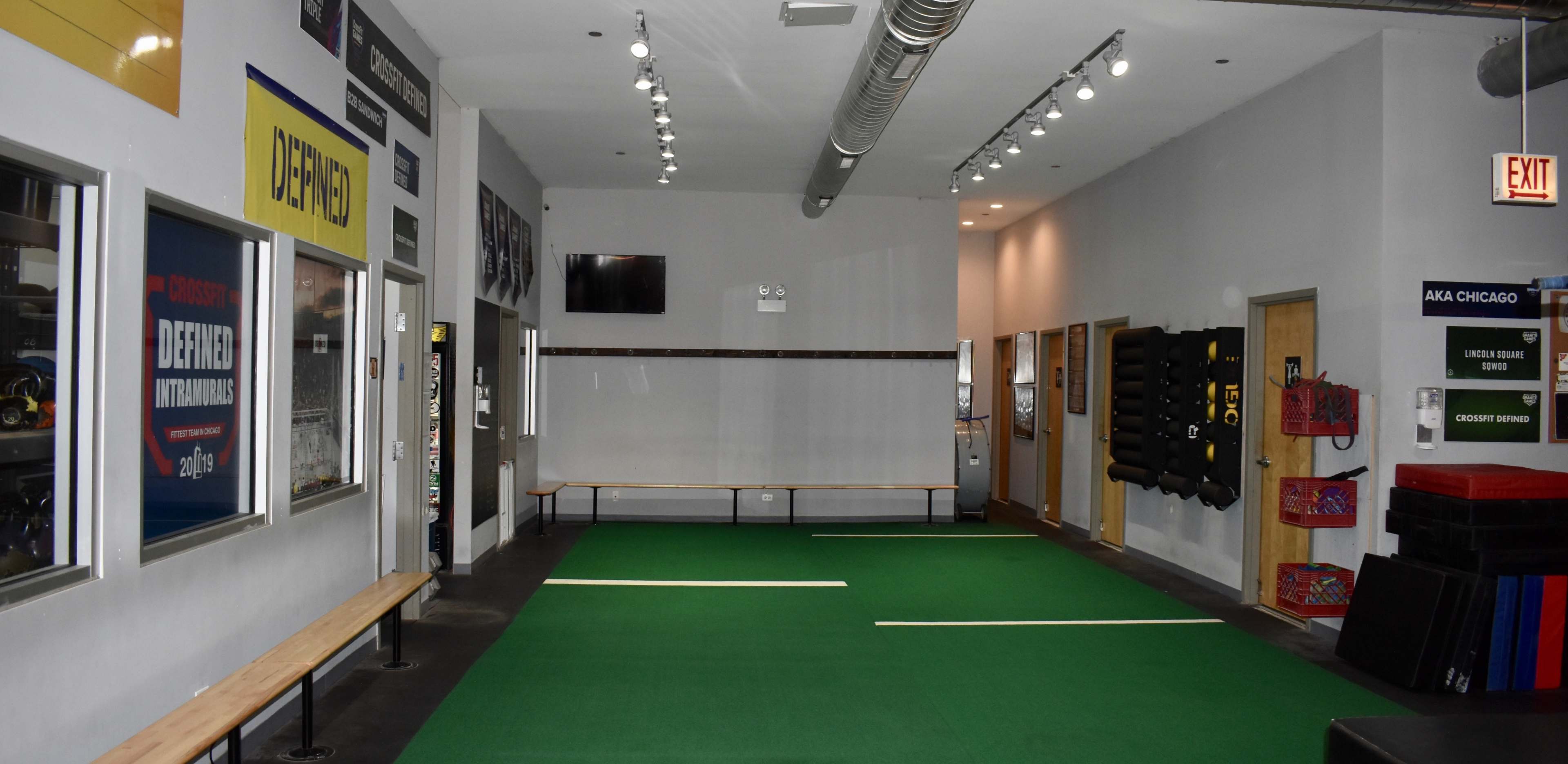 A gym or training facility with a green turf area in the center, flanked by walls displaying various signs and equipment.