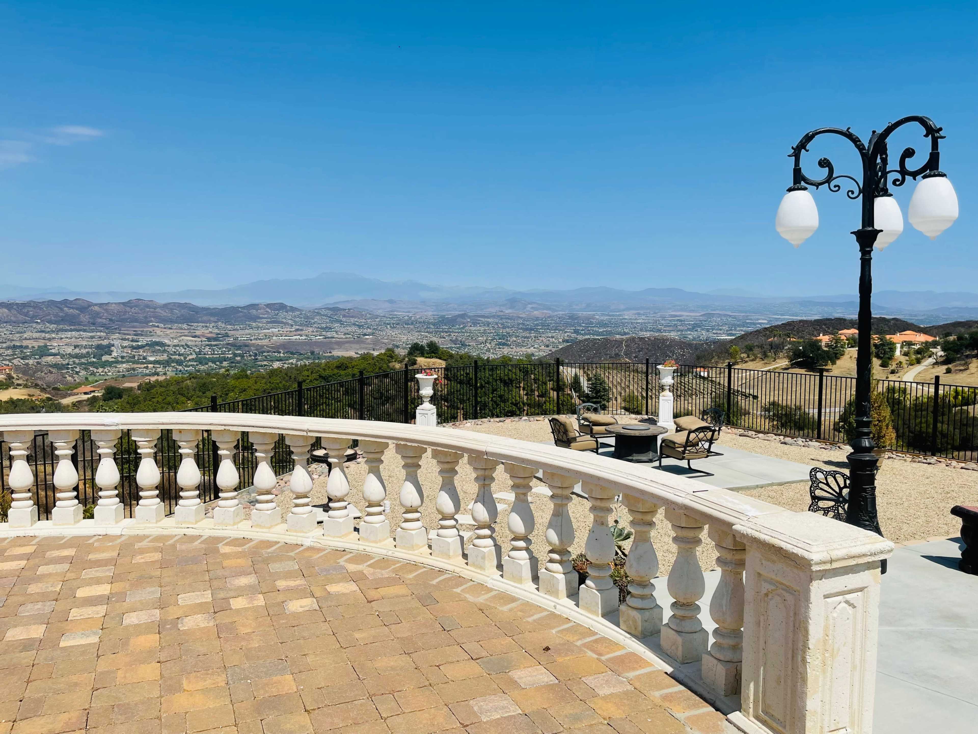 A terrace with a balustrade overlooking a valley and mountains under a clear blue sky.