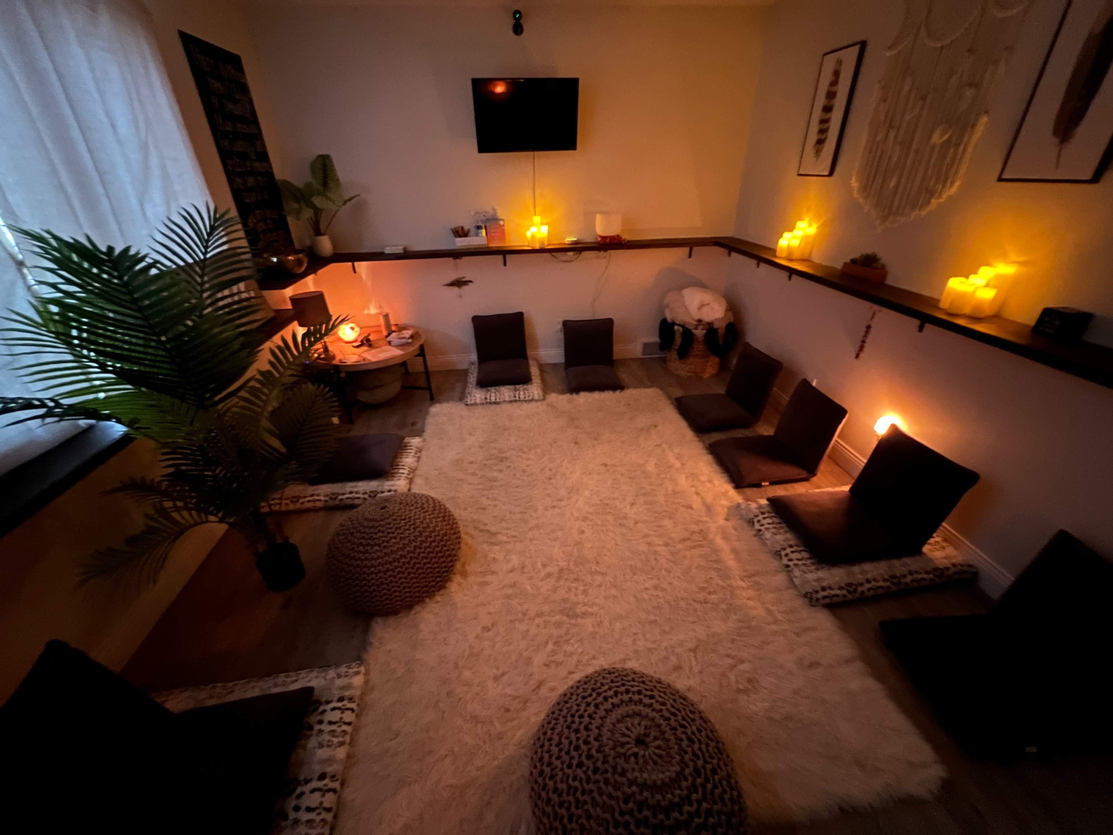 A cozy room arranged with floor cushions and a large rug, illuminated by soft candlelight.