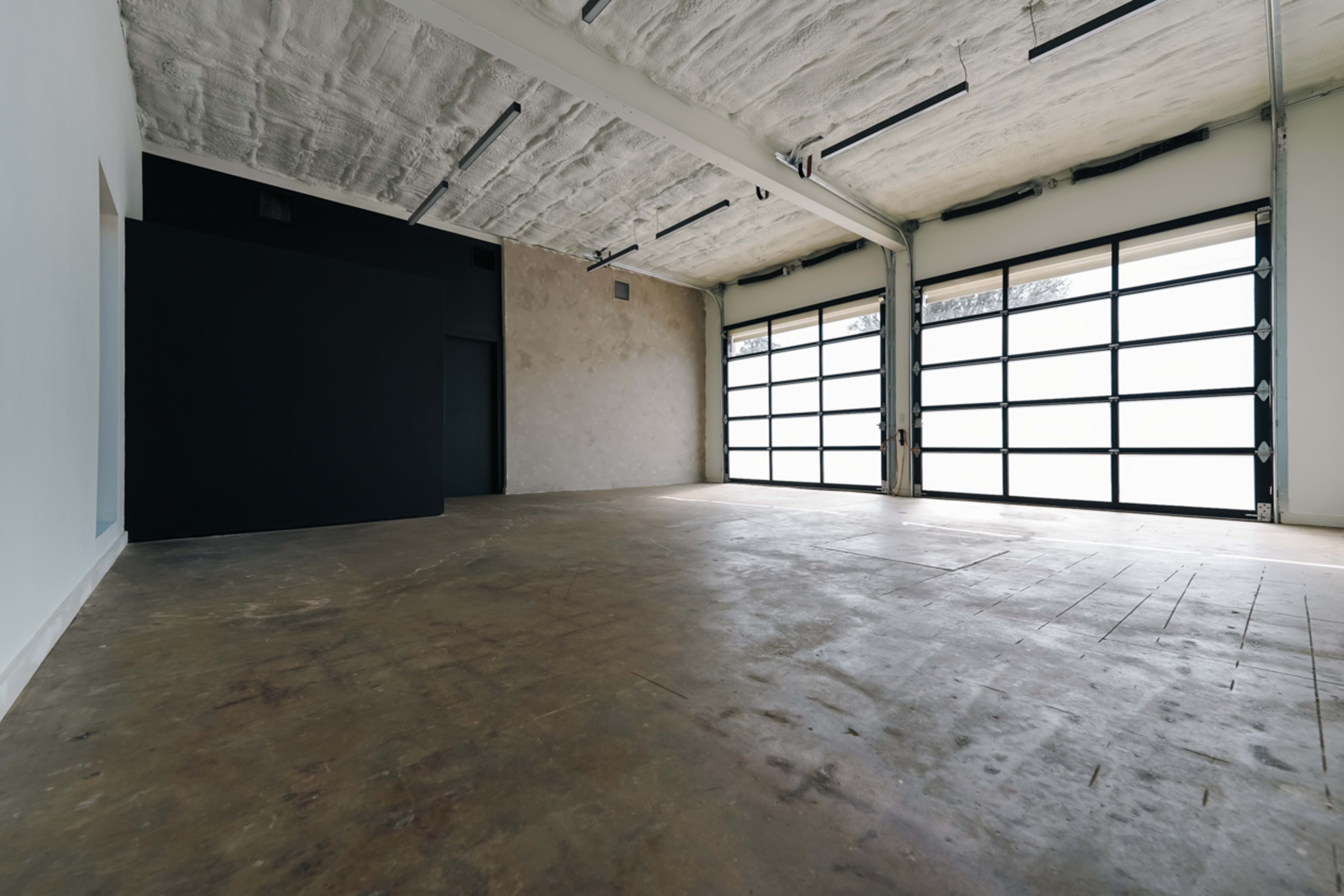 A spacious, empty industrial-style room with large glass doors on one side and a dark wall on the opposite side.