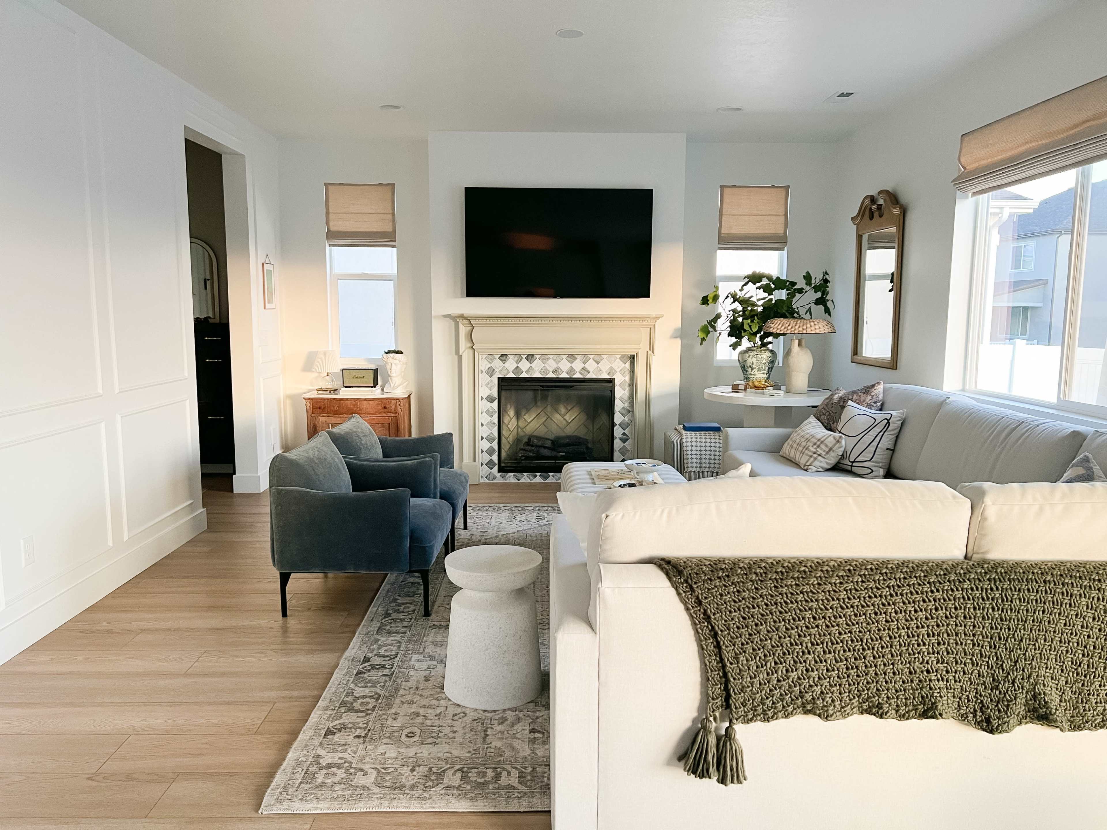 A modern living room featuring a fireplace with a large television above it, a light-colored sofa, and a coffee table surrounded by chairs.