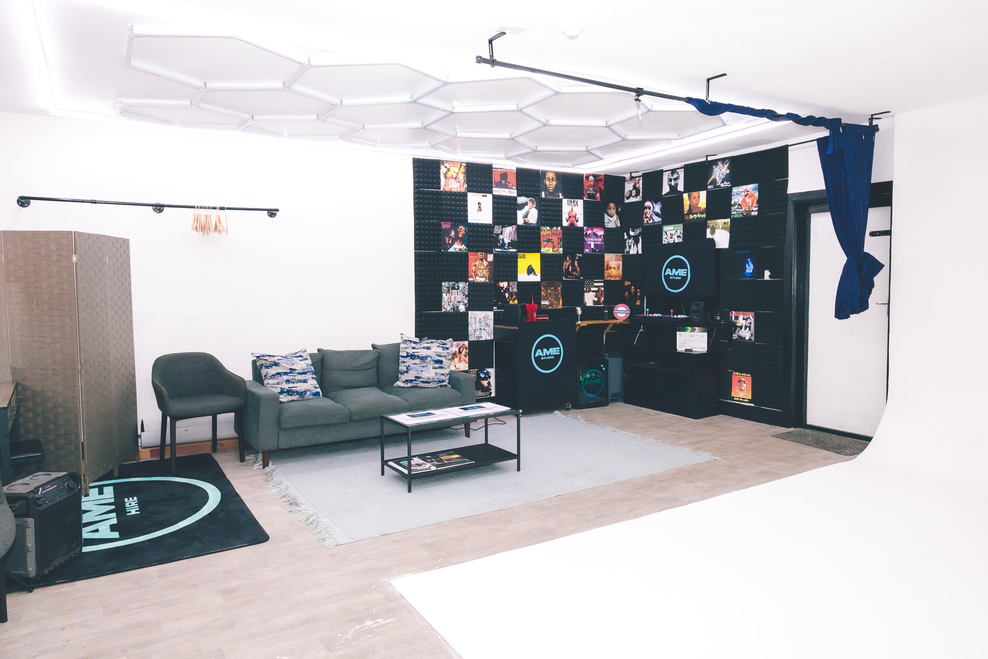 The image shows a modern studio space with a seating area, a wall covered in framed artworks, and a backdrop for photography.