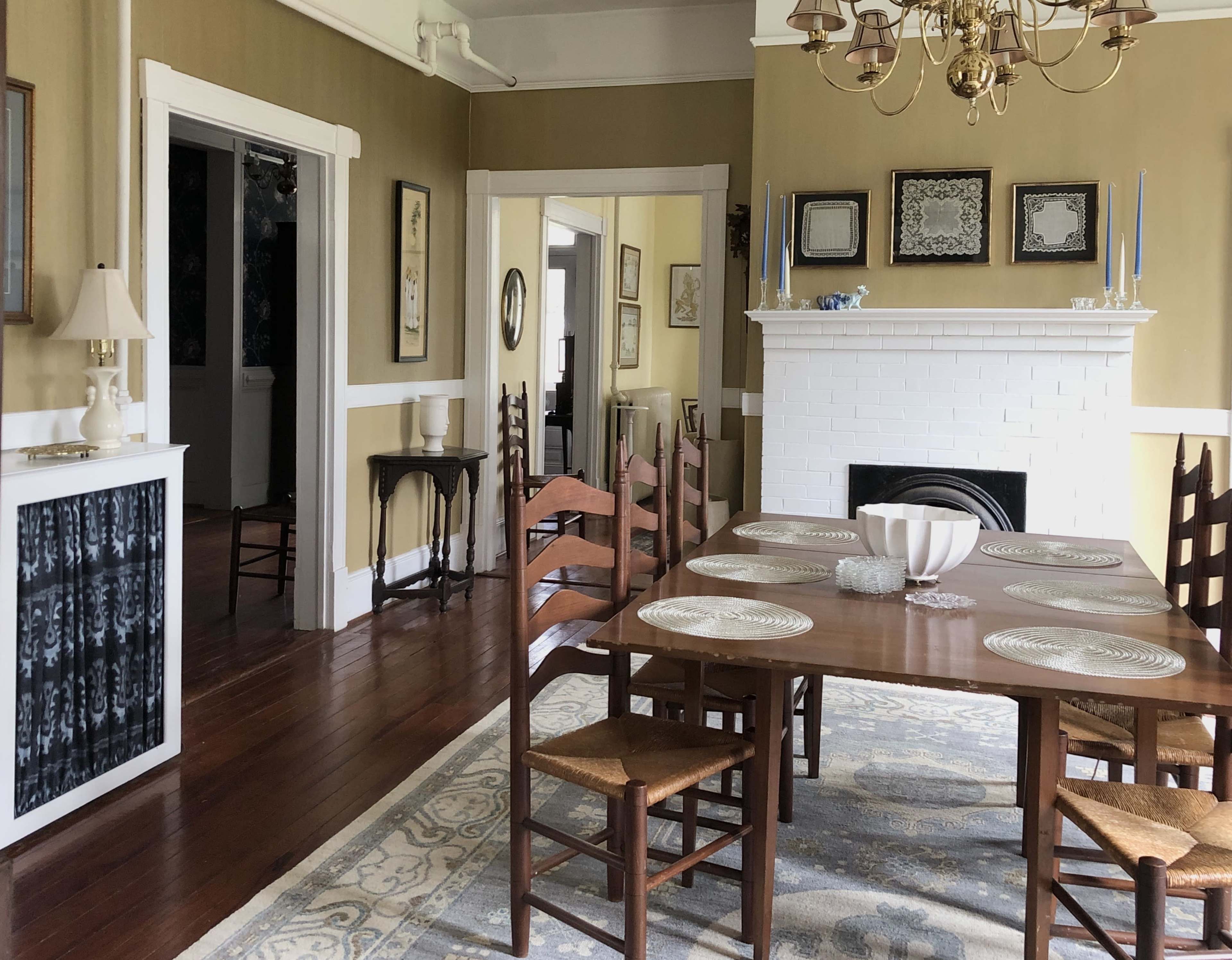 The image shows a dining room with a wooden table set for a meal, surrounded by chairs, and featuring a fireplace with decorative items on the mantel.