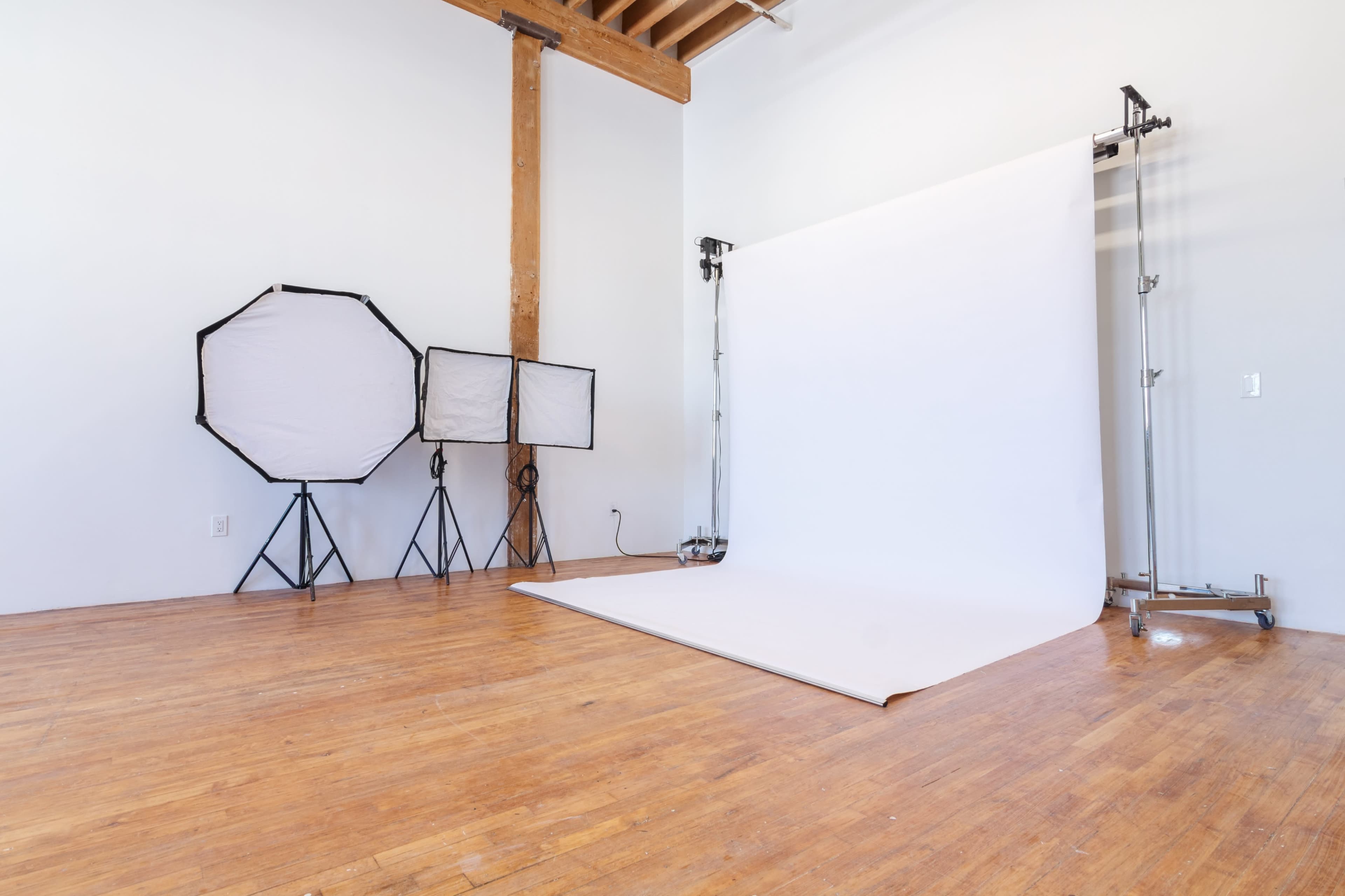 A photography studio with a blank backdrop, lighting equipment, and wooden flooring.
