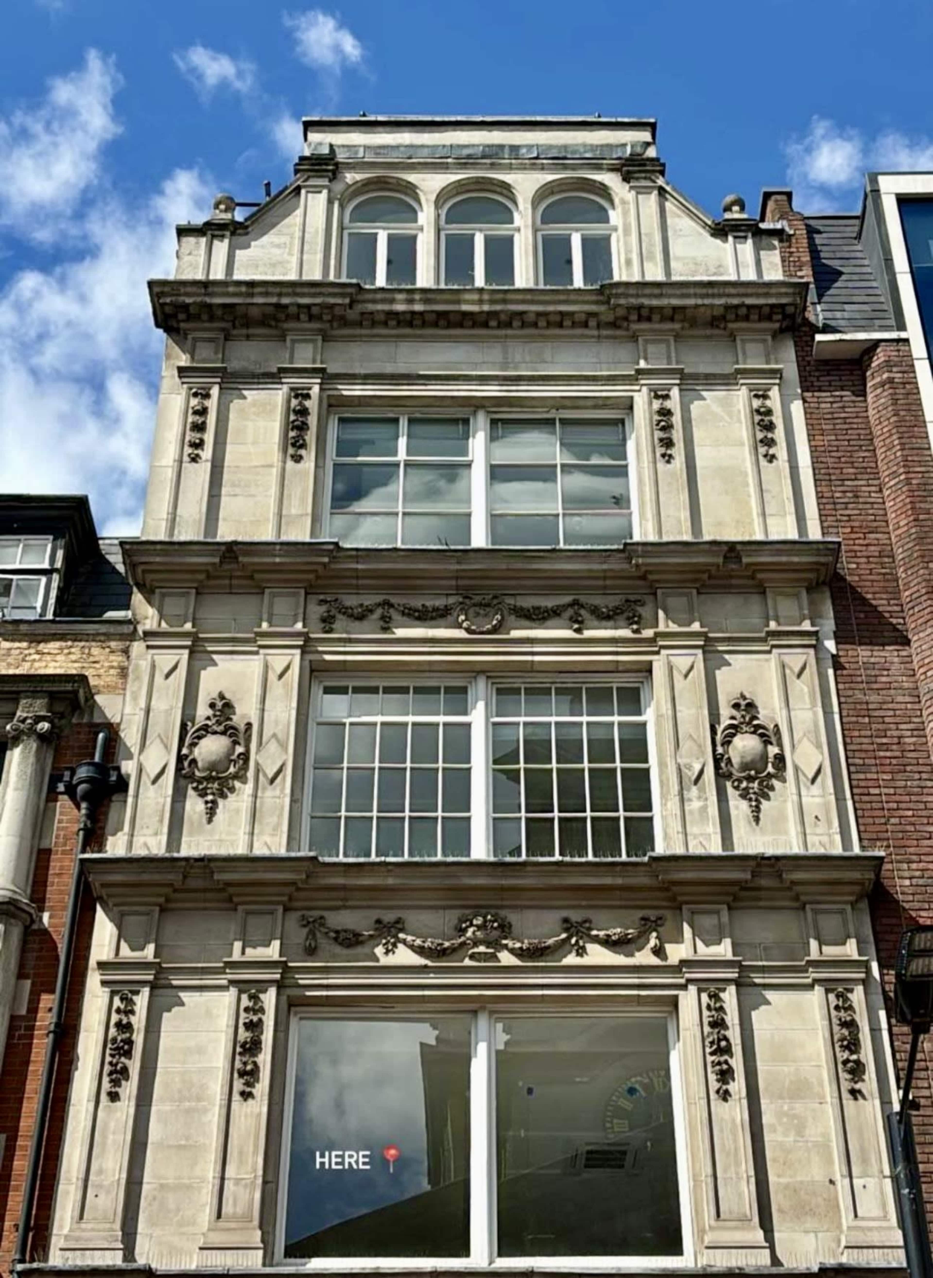 A decorative building facade featuring ornate details and large windows on the upper levels under a blue sky with scattered clouds.