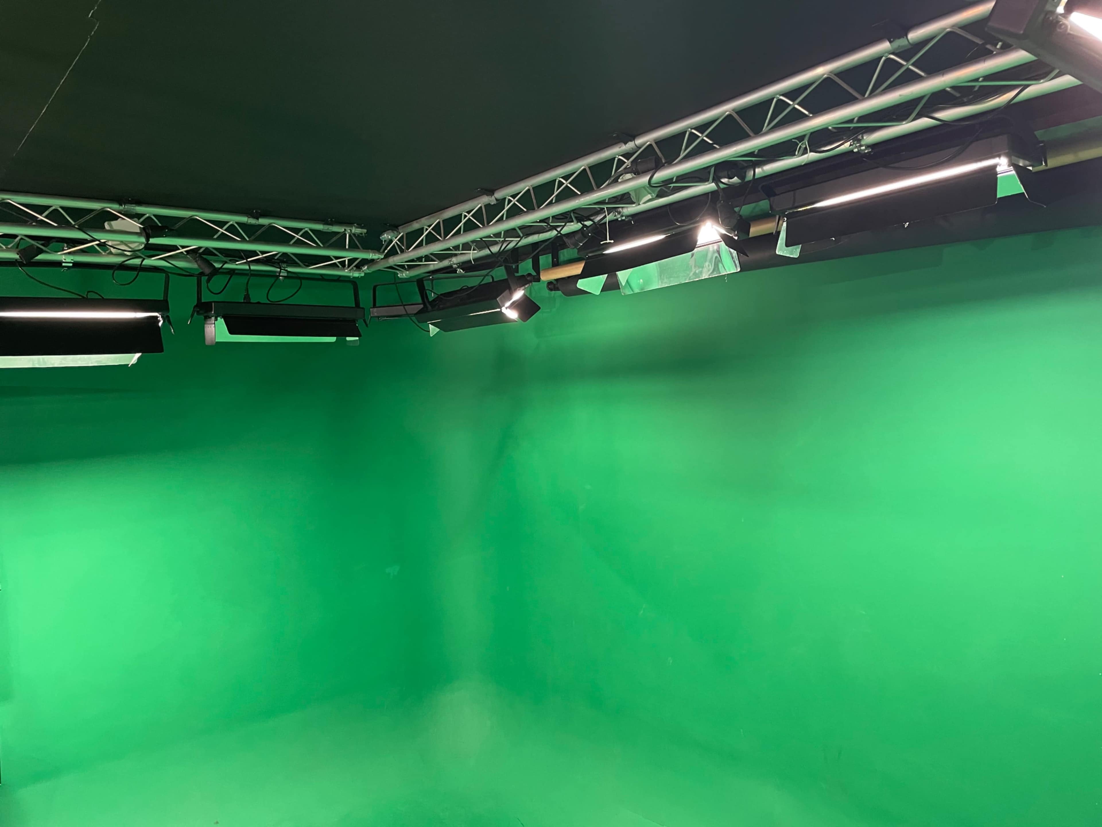 The image shows a green screen studio with overhead lighting and a bare green backdrop.