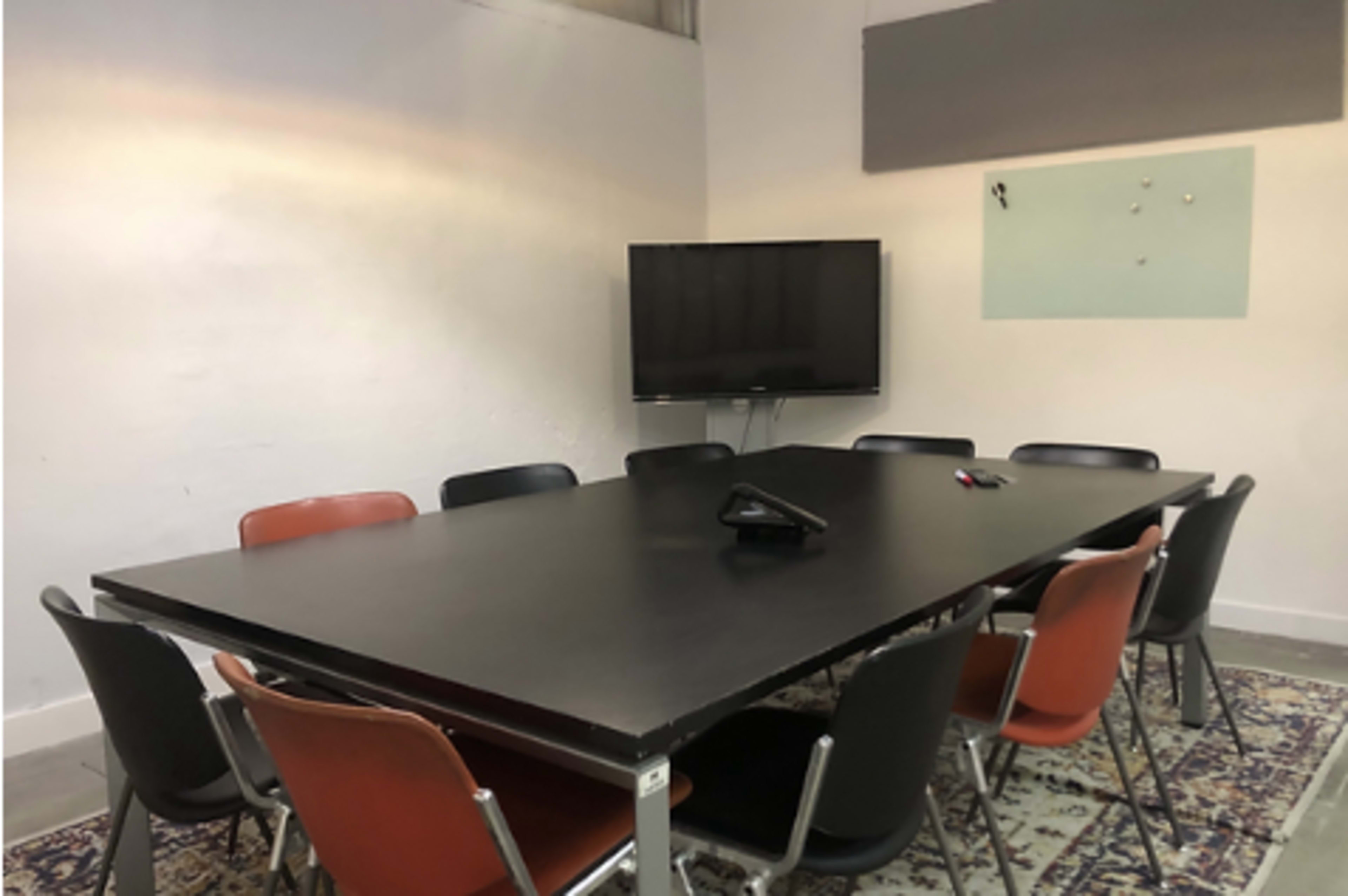 A conference room with a large black table surrounded by several chairs and a television mounted on the wall.