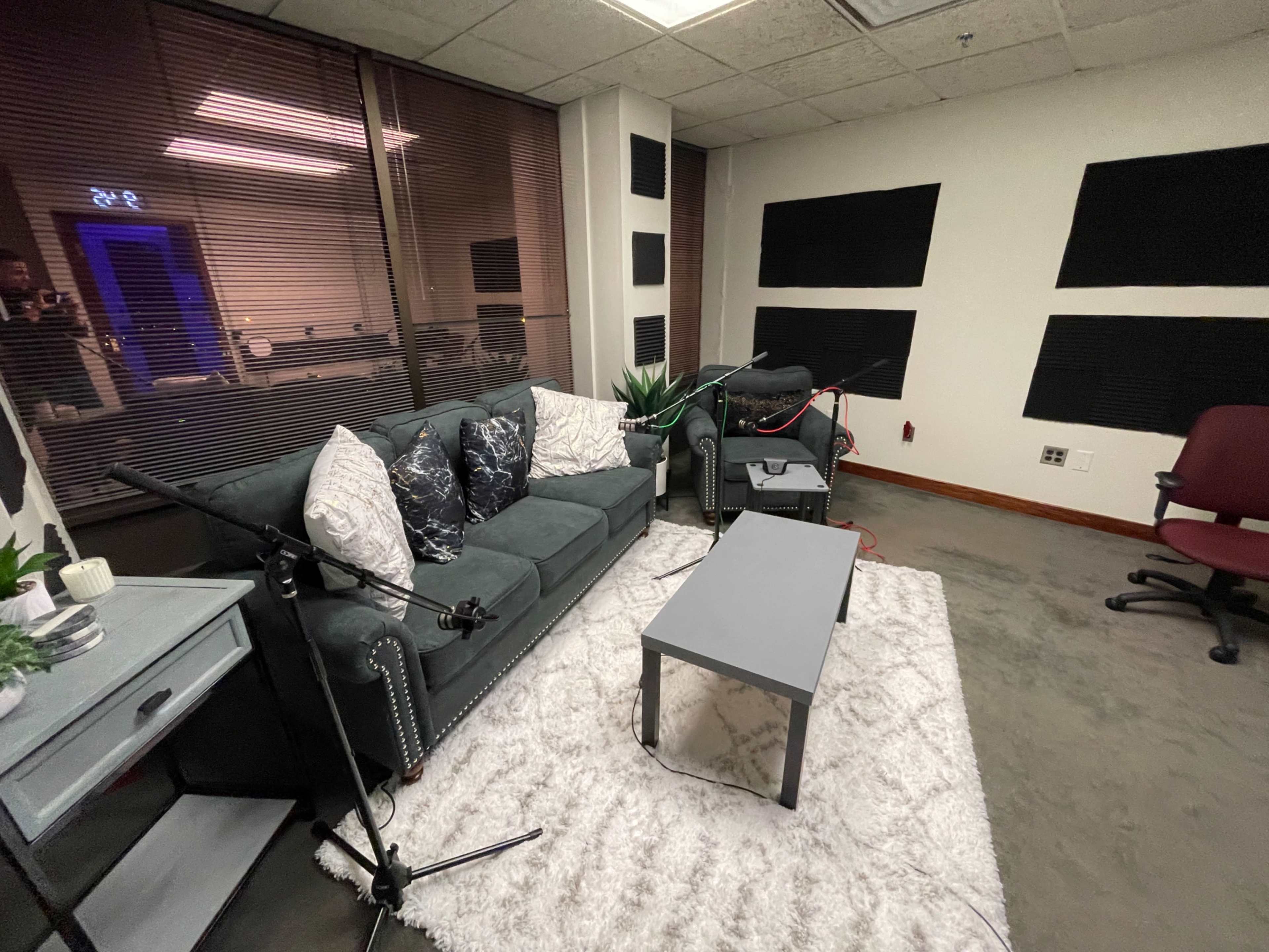 A small recording studio with a green couch, a gray coffee table, and soundproofing panels on the walls.