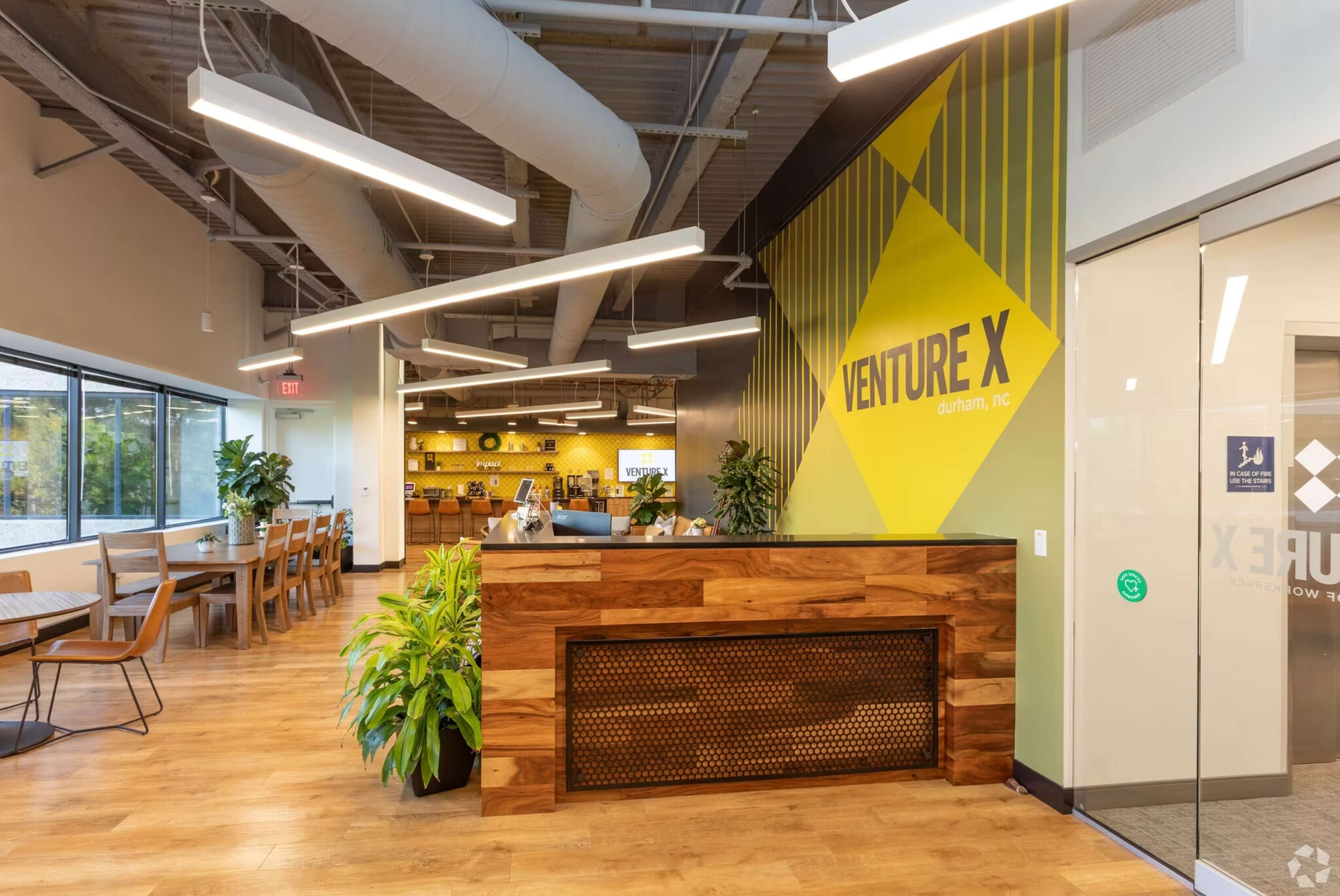 A modern office reception area with a wooden front desk, large windows, and decorative plants.
