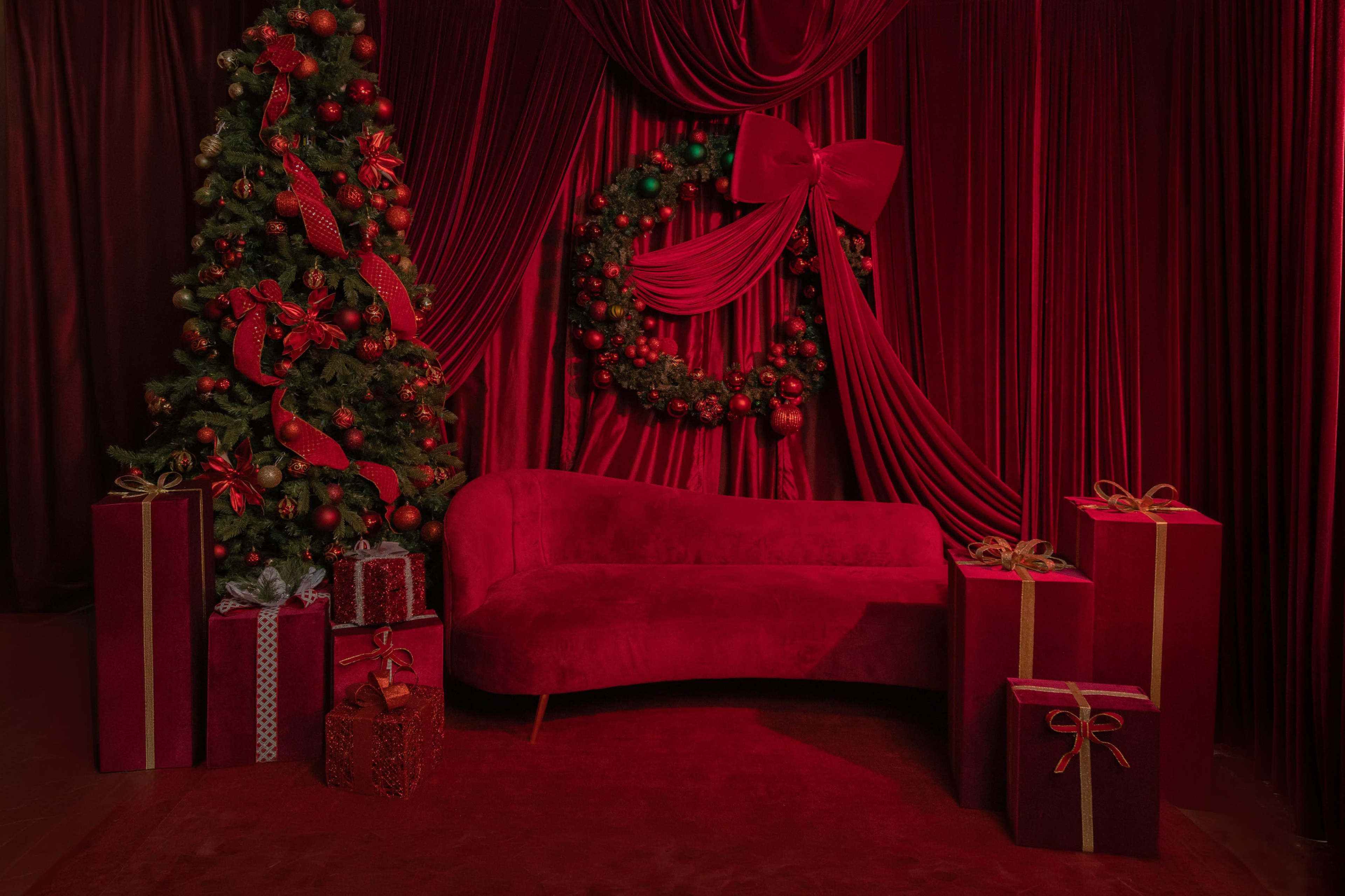 The scene features a red-themed holiday setup with a decorated Christmas tree, a wreath, red drapery, and several gift boxes arranged around a red couch.