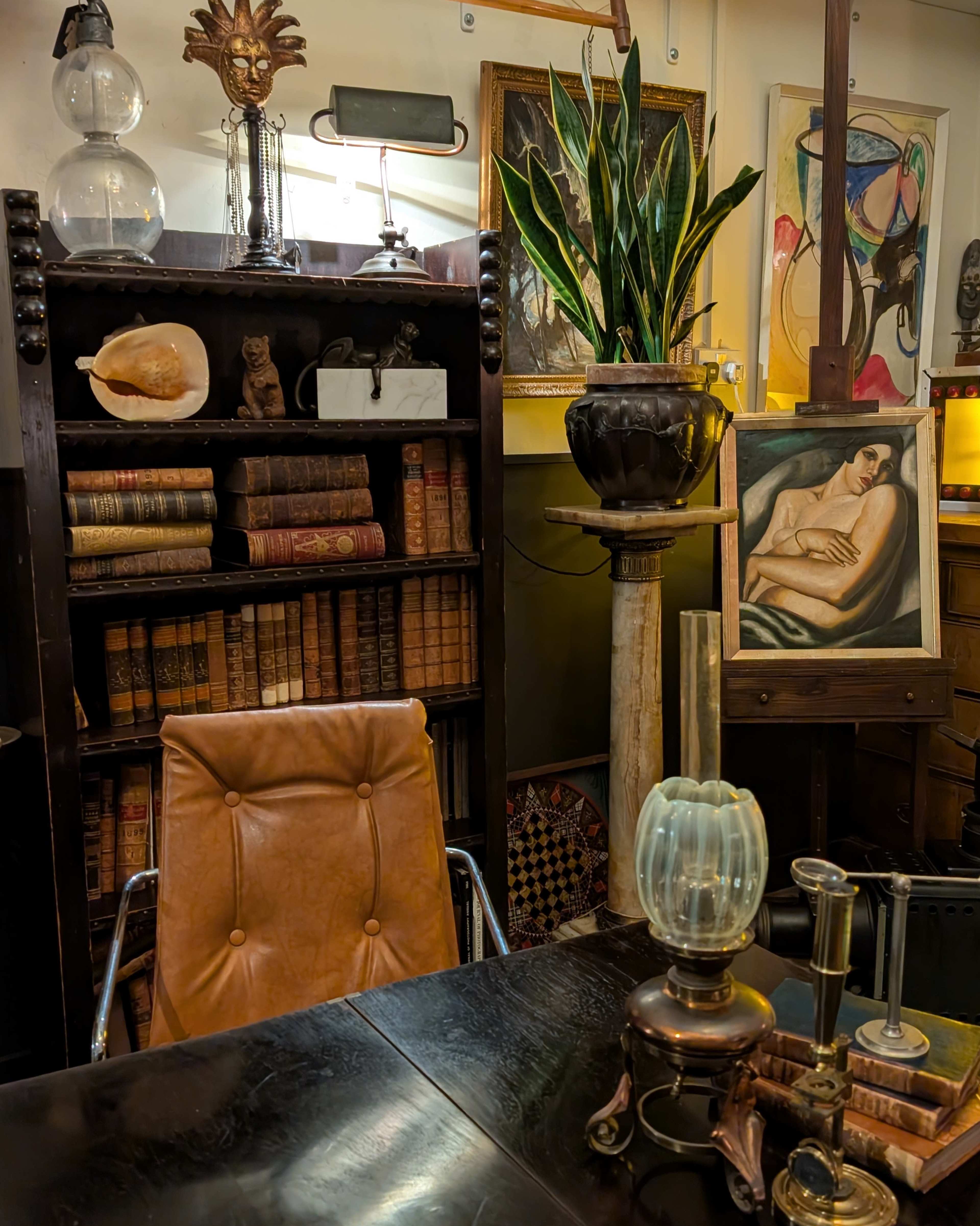 The image features a vintage study or office space with a leather chair, a wooden bookshelf filled with old books, a potted plant, and various artistic elements including a painting and unique decorative items.