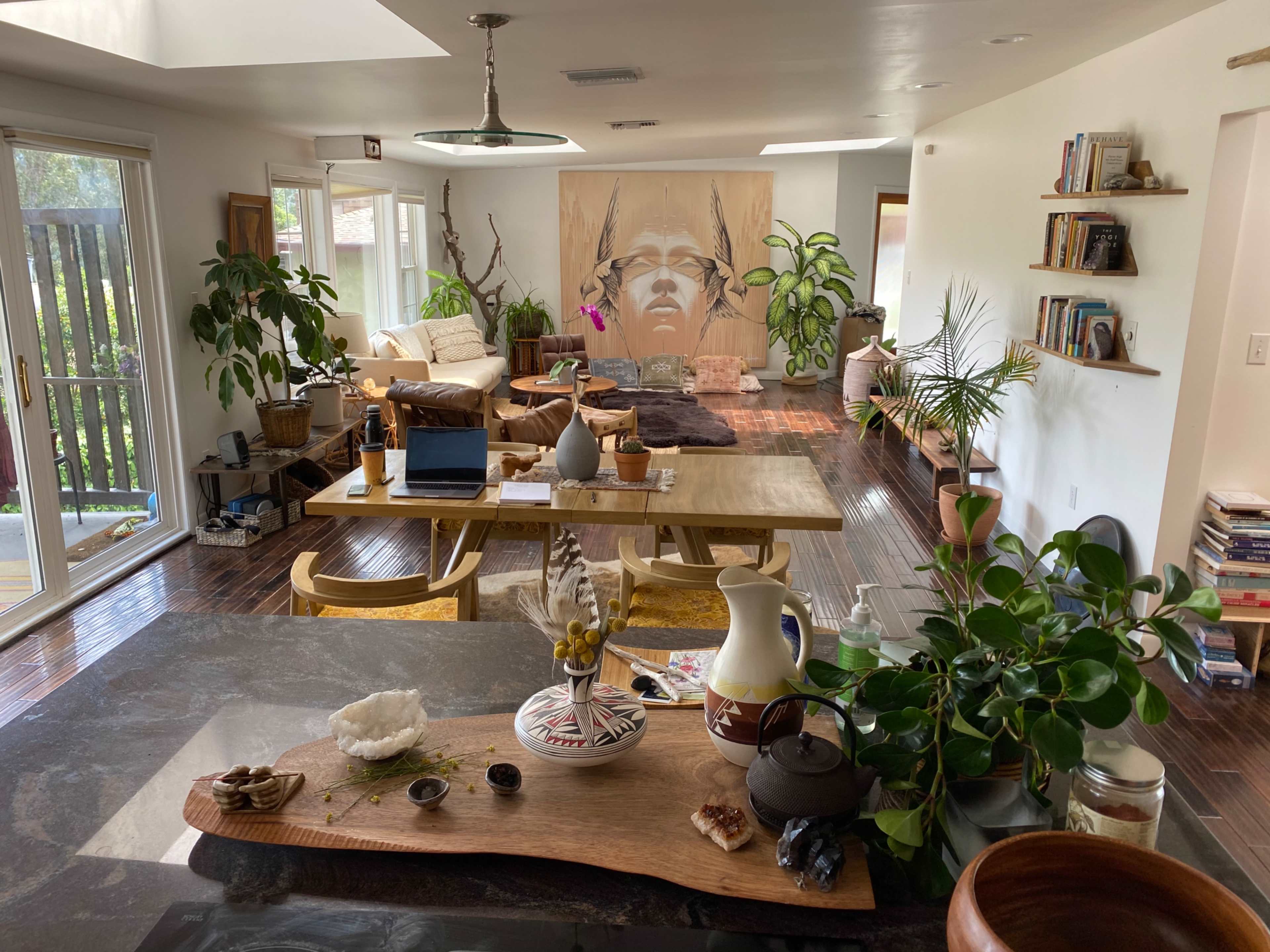 A bright, airy living space featuring a dining area, plants, and a large artwork of a Native American figure on the wall.