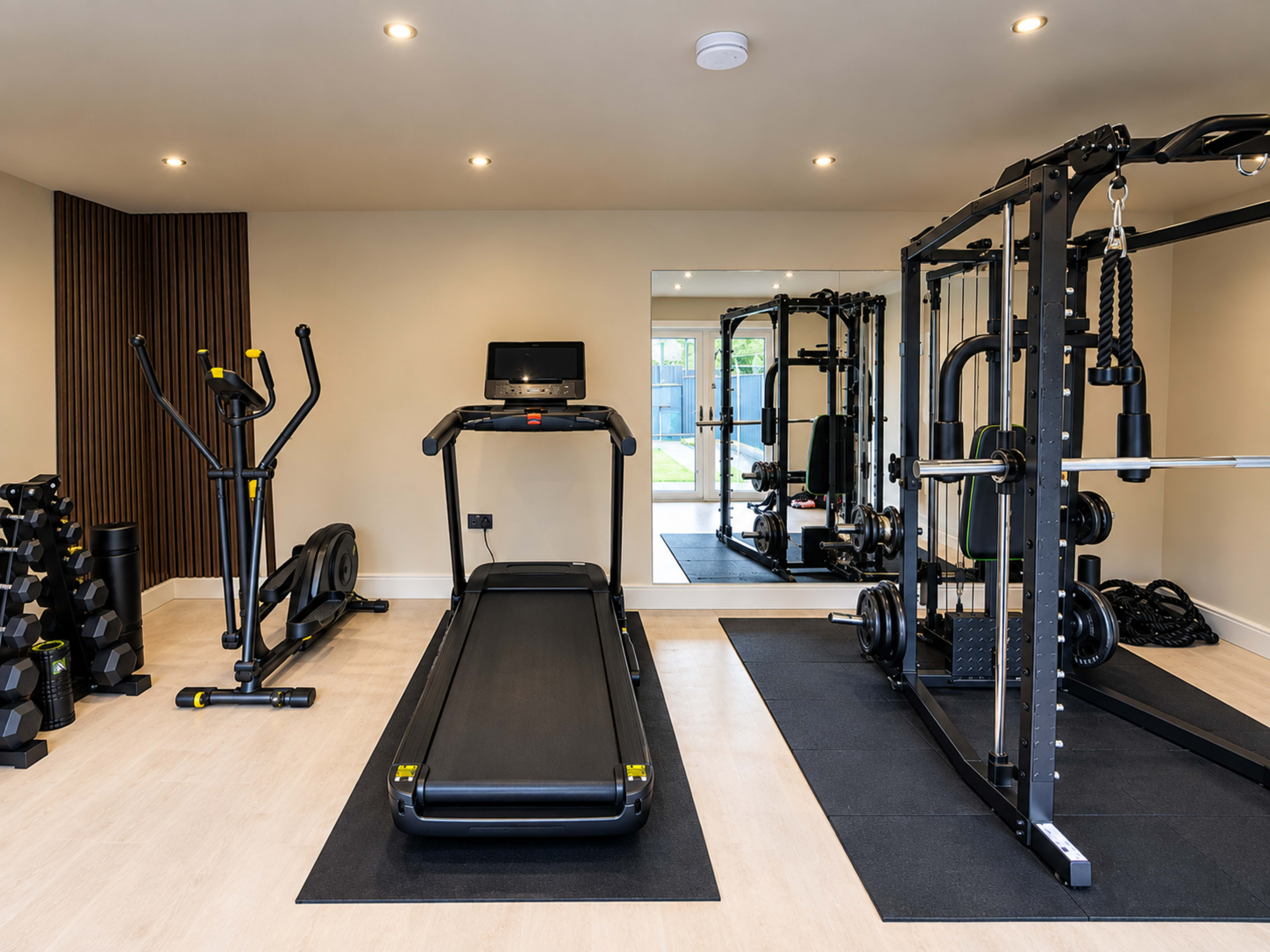 The image shows a modern gym interior featuring a treadmill, a multi-functional weightlifting machine, and a set of free weights.