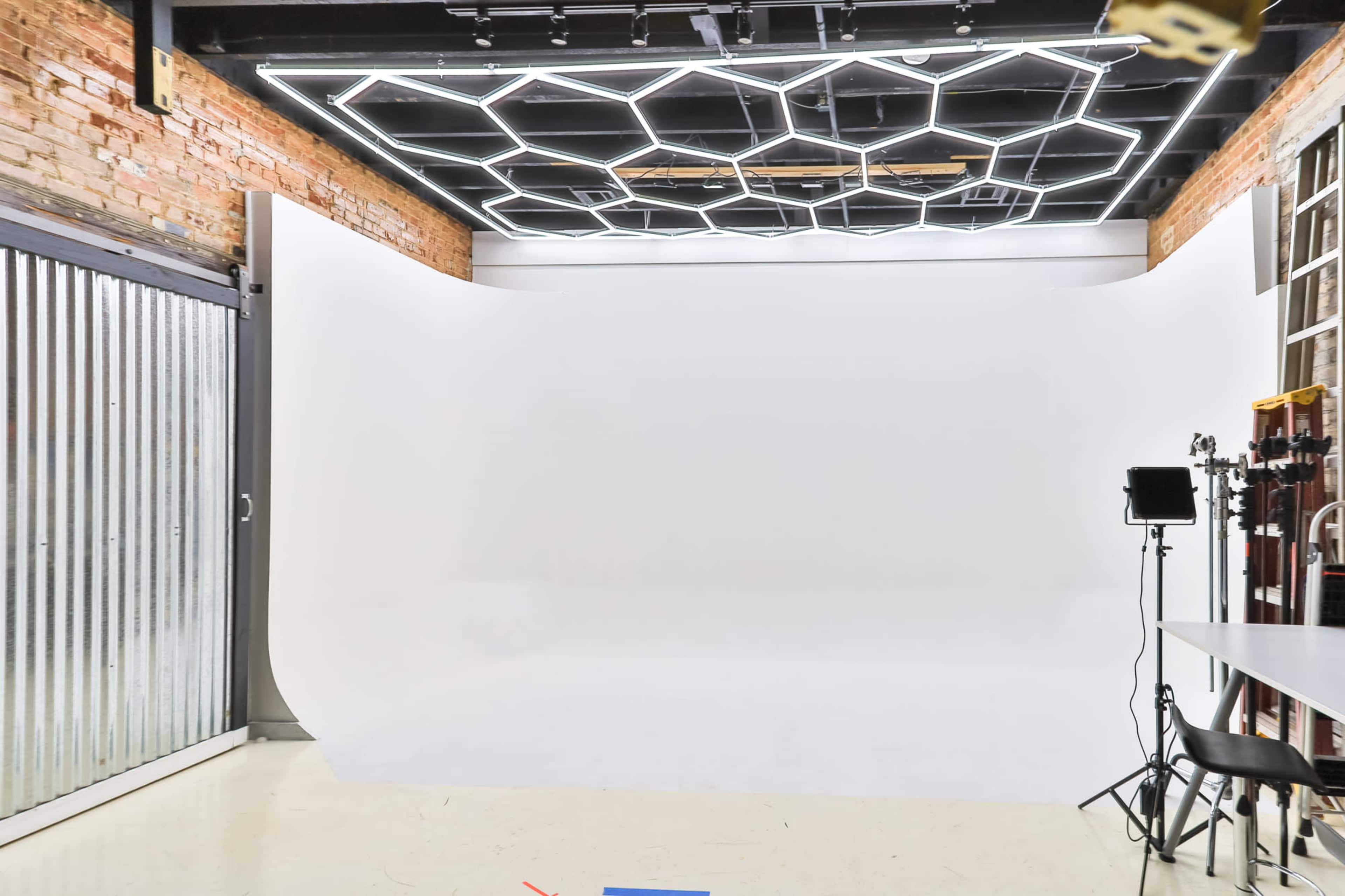 The image shows a photography studio with a large white backdrop, a hexagonal light fixture on the ceiling, and a metal door on one side.