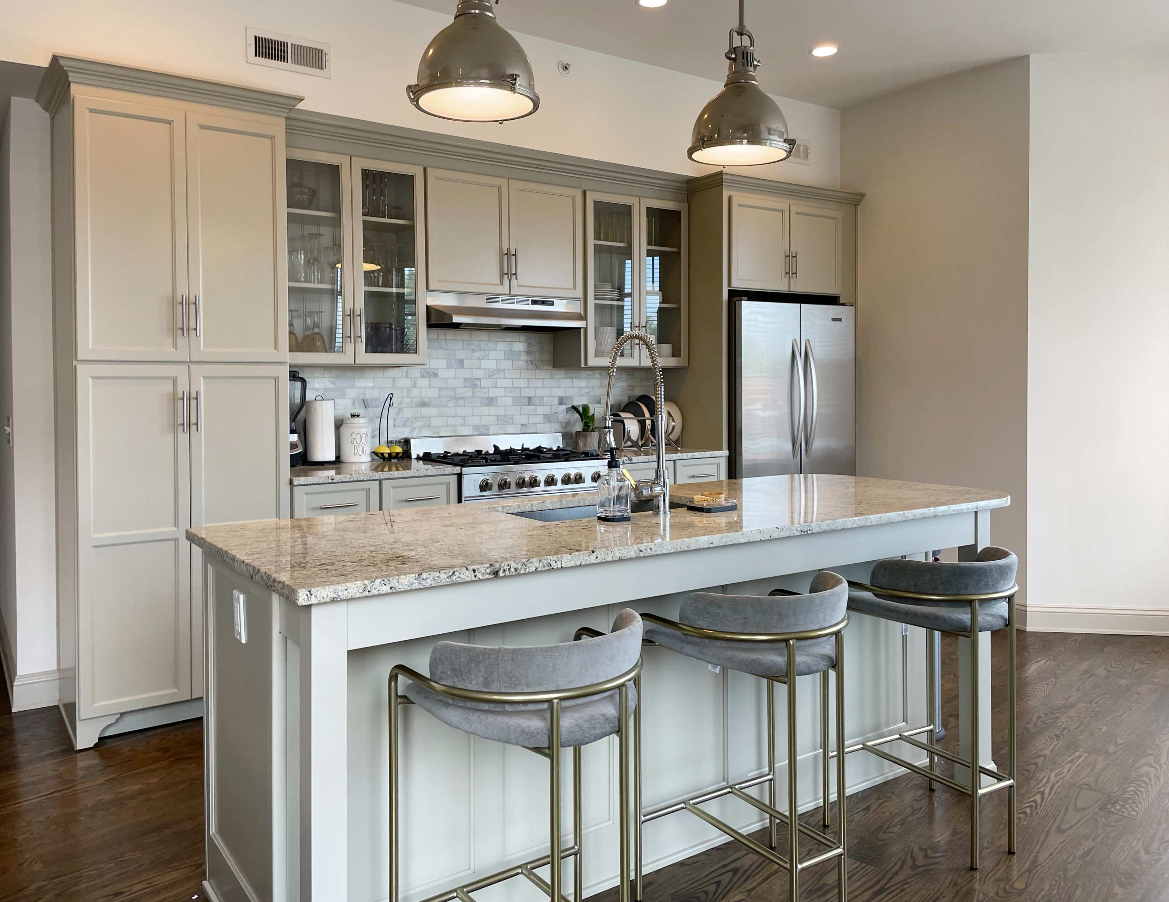 A modern kitchen features a large island with bar stools, grey cabinets, stainless steel appliances, and a white marble countertop.