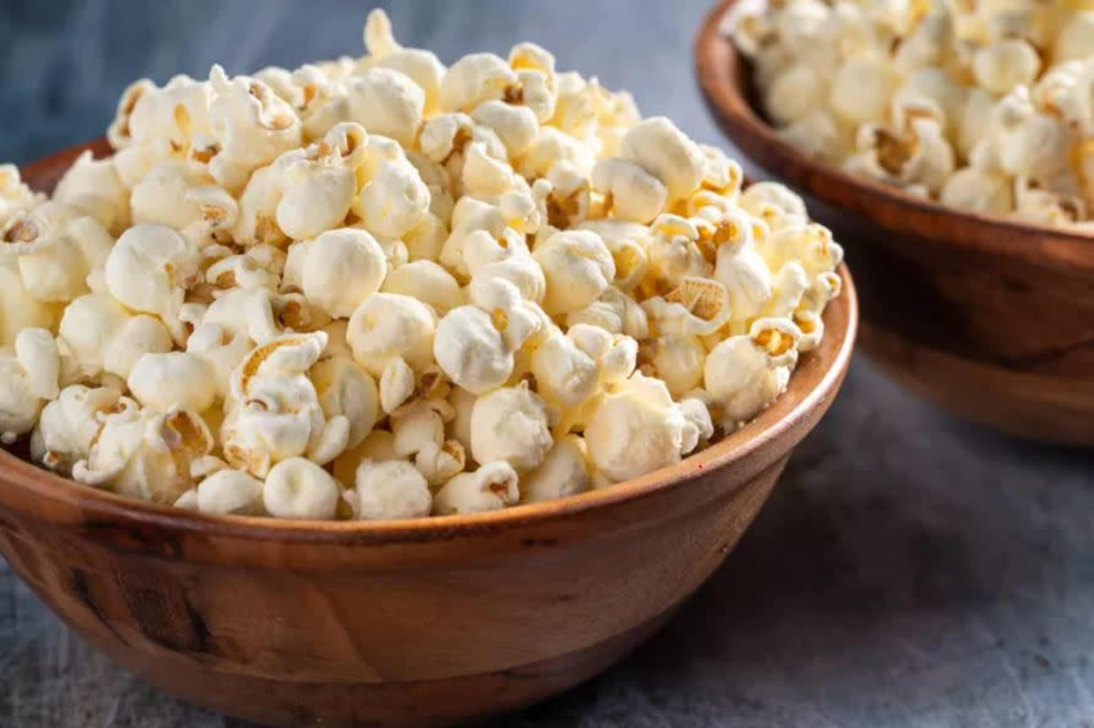 Two wooden bowls filled with freshly popped popcorn are placed on a textured surface.
