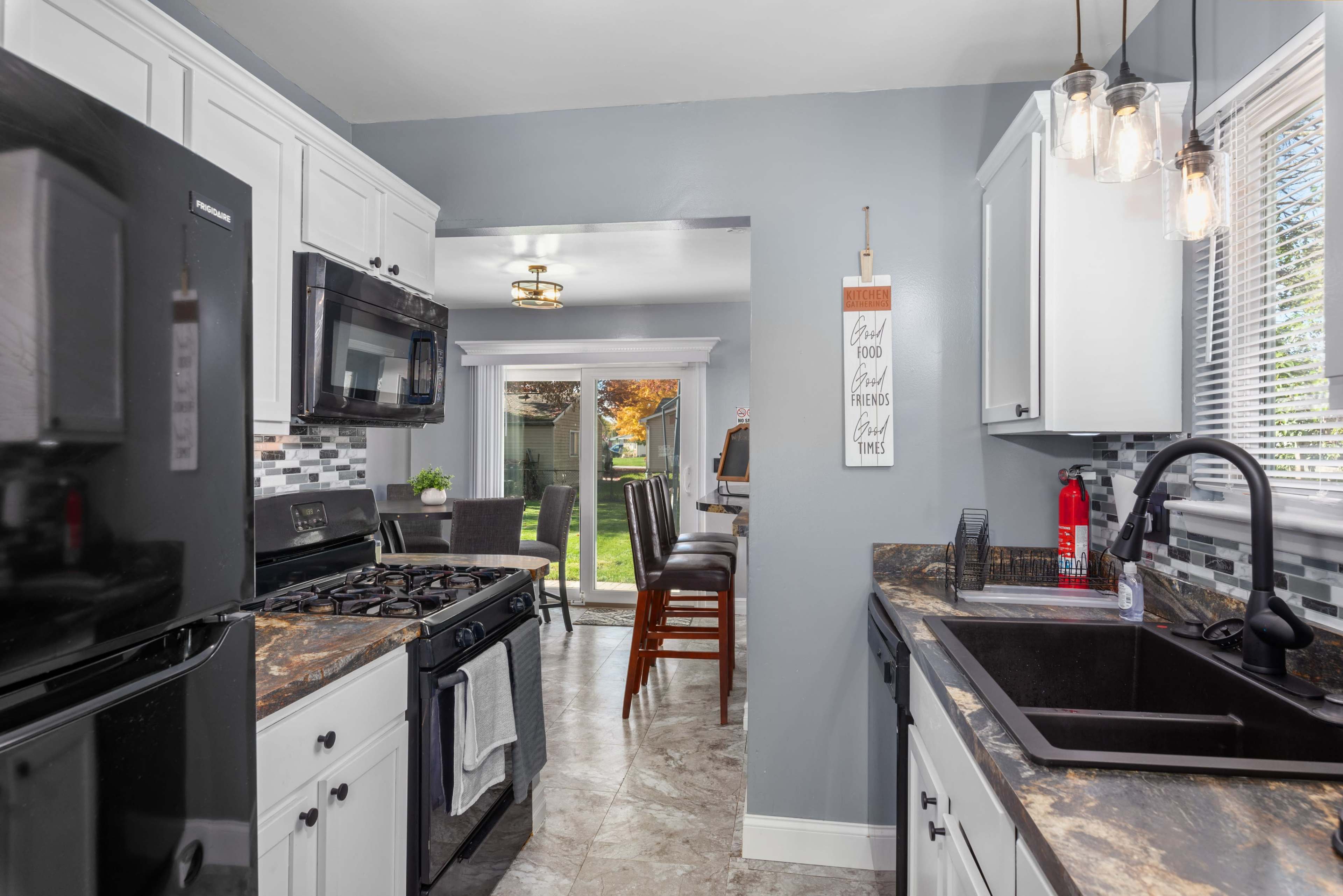 A modern kitchen with black appliances, white cabinets, and dark countertops, leading to a patio visible through glass doors.