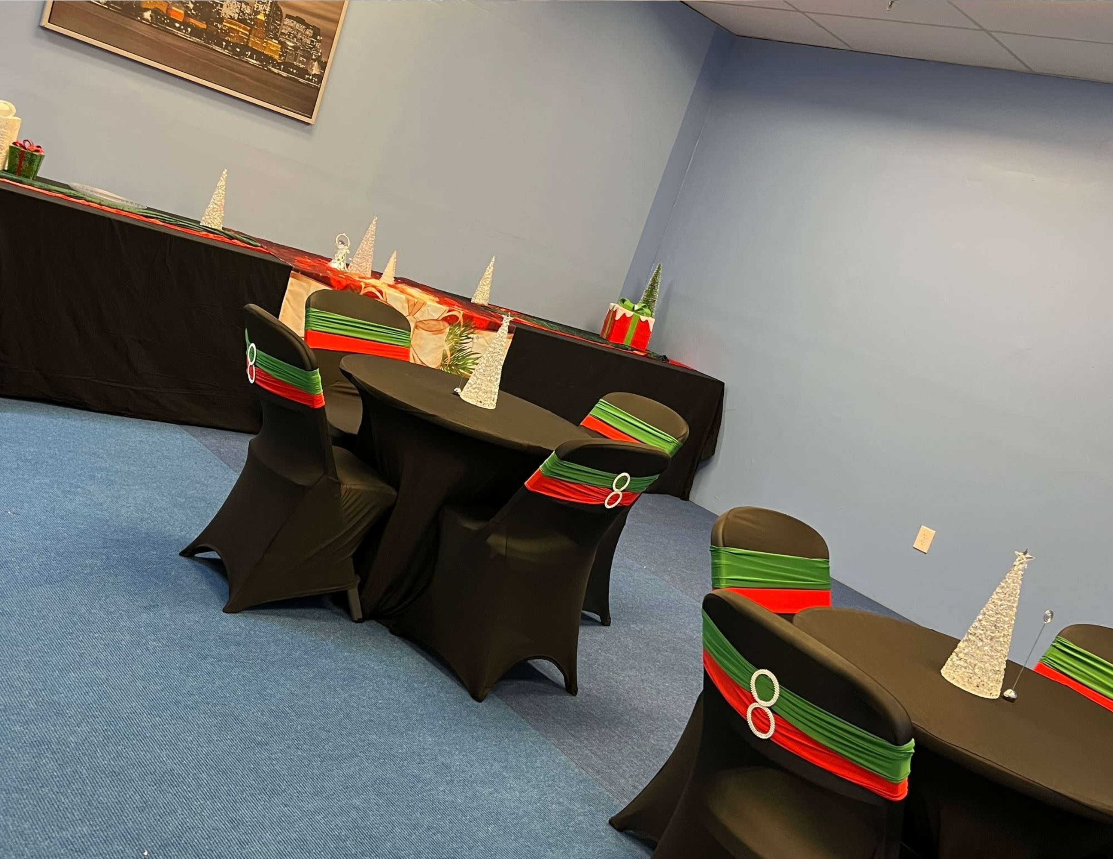 The image shows a decorated room with black tables covered in red and green accents, featuring small Christmas tree decorations and a buffet table in the background.