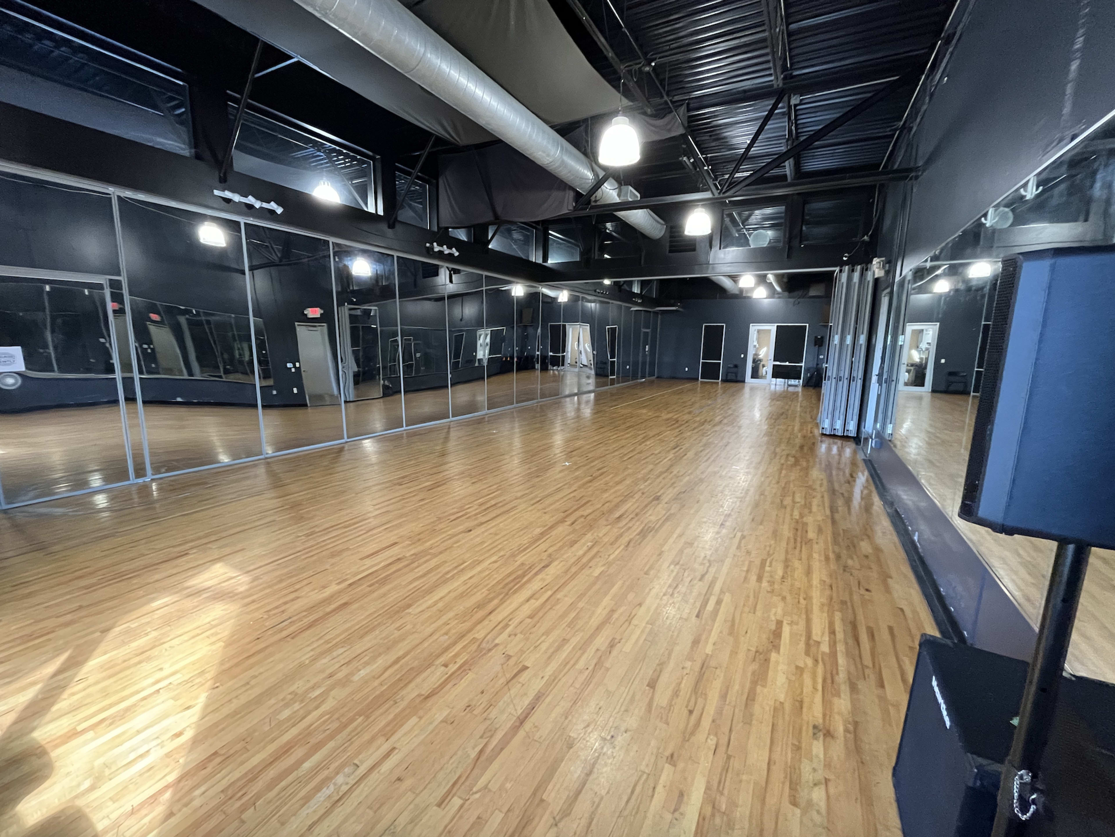 The image shows a spacious dance studio featuring a polished wooden floor and large mirrors lining one wall.