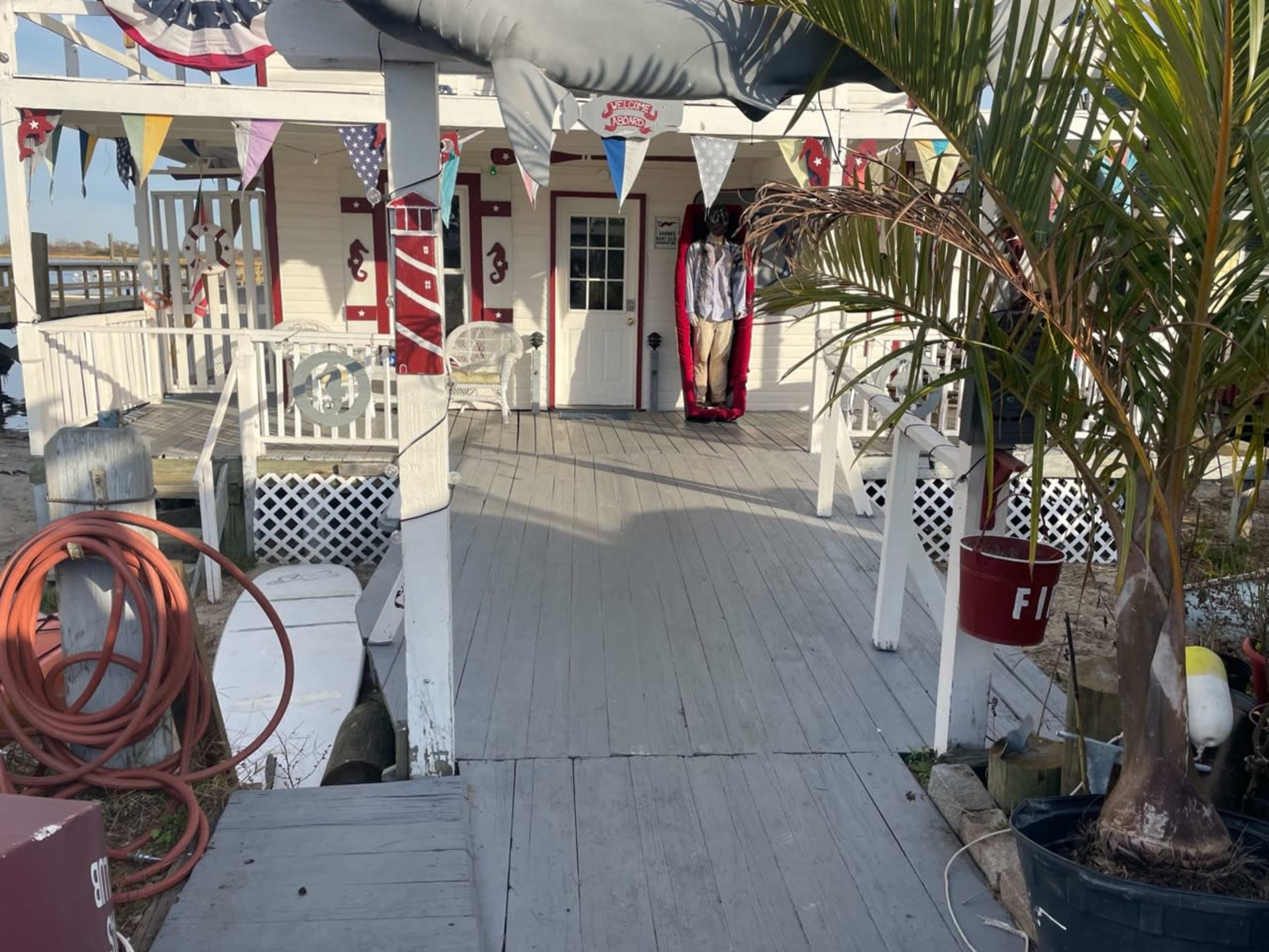 A wooden walkway leads to a decorated building with patriotic banners and a person dressed in a red and white outfit standing at the entrance.