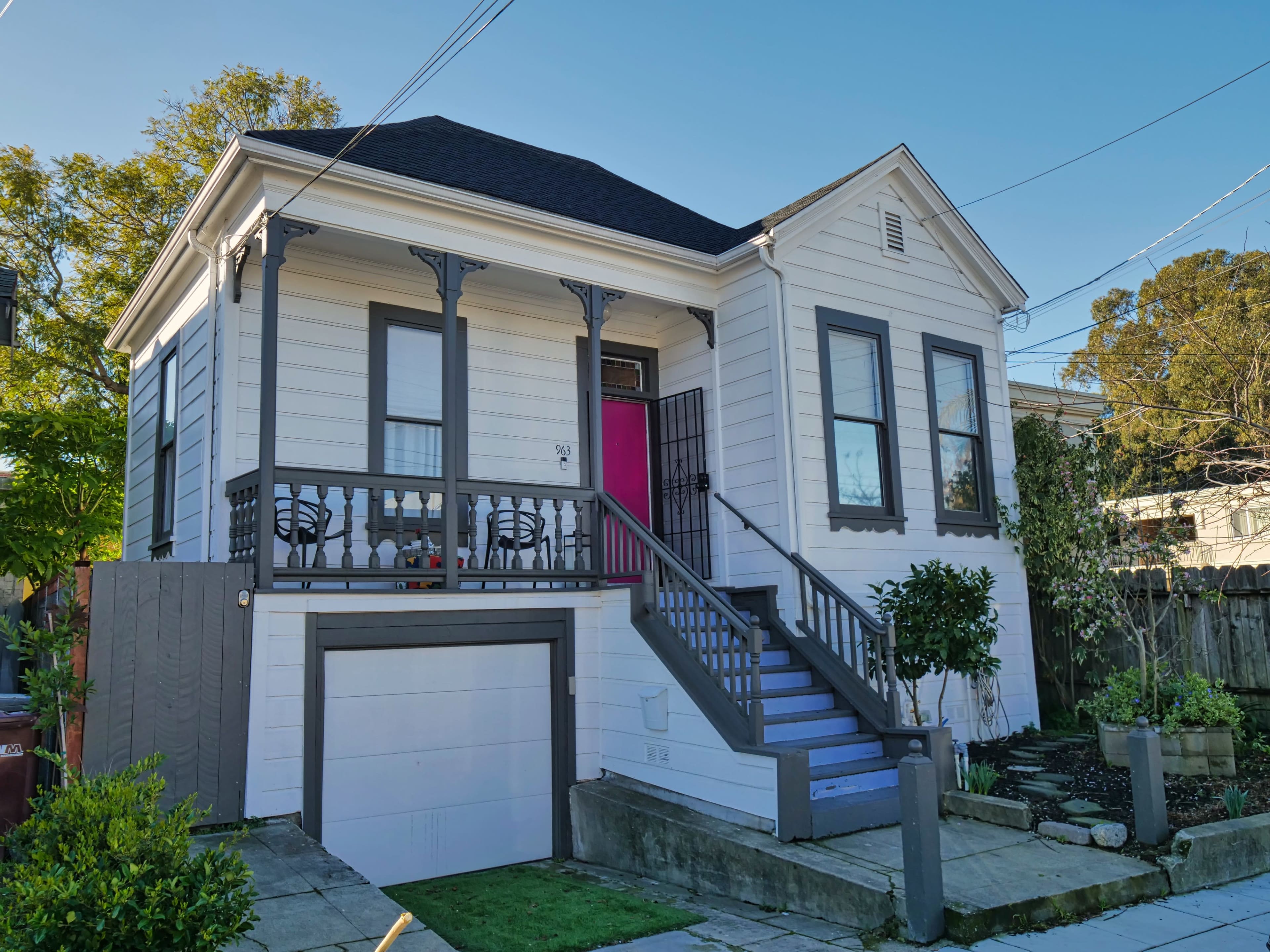 The image shows a two-story white house with a front porch, purple stairs, and a garage on the left side.