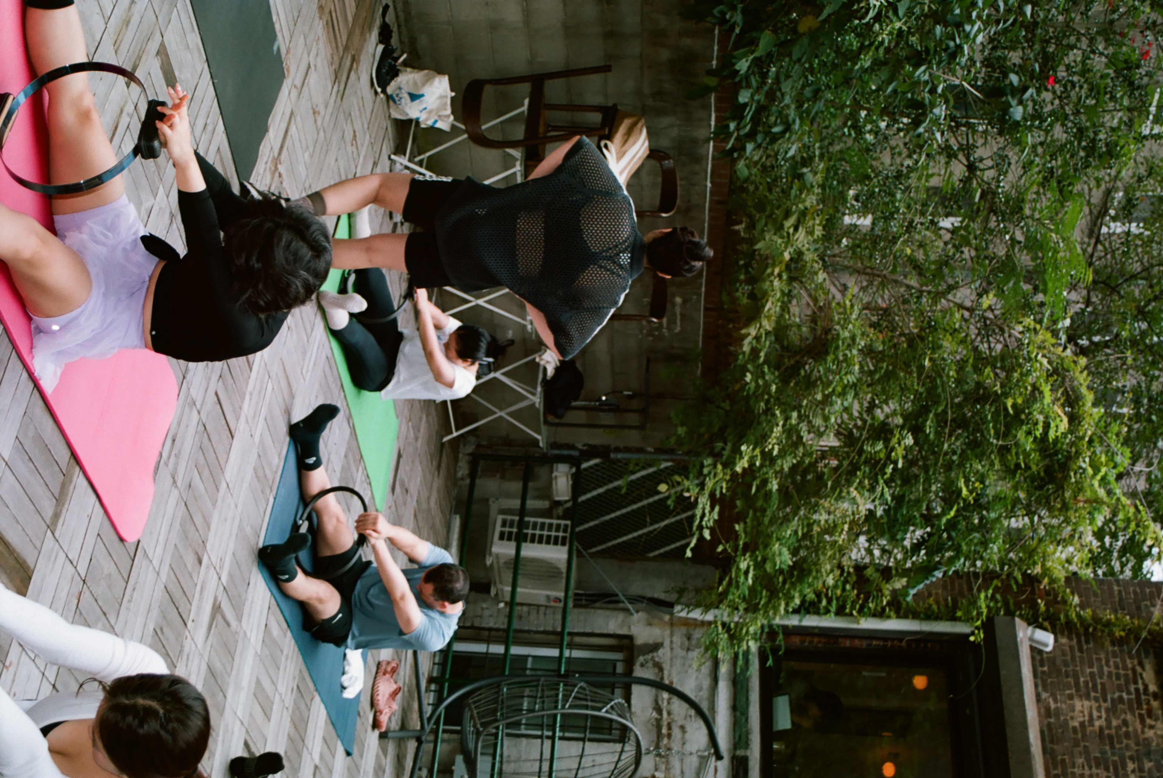 A group of people are participating in a yoga or fitness class on a wooden deck lined with exercise mats.