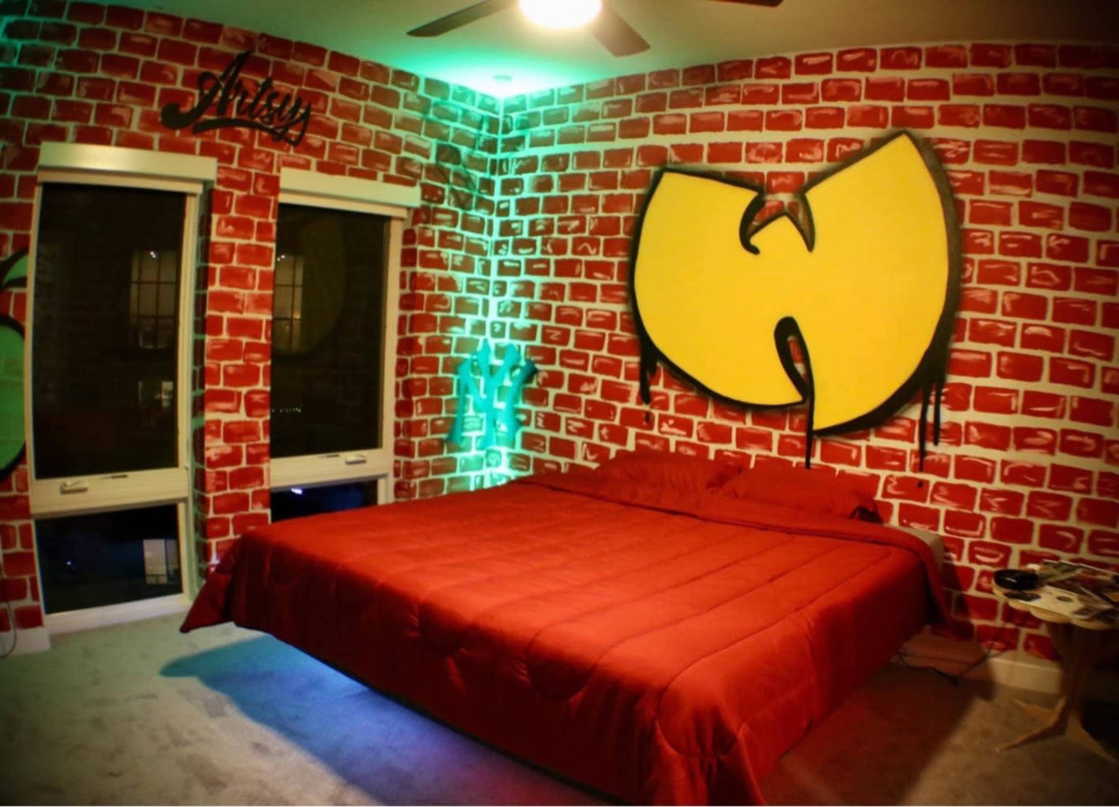 A bedroom with red brick-patterned walls, a yellow Wu-Tang Clan logo, and a red bedspread.