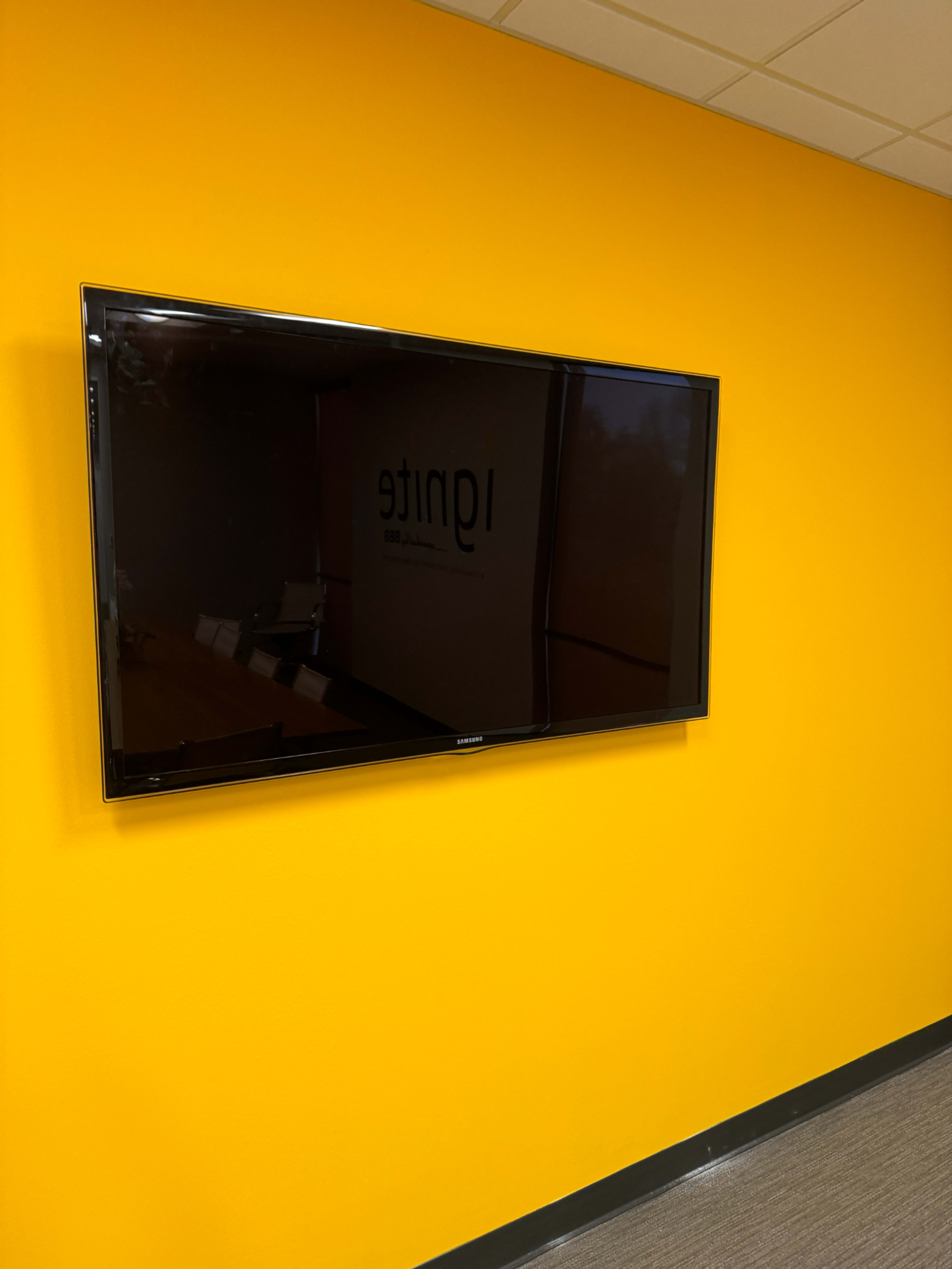 A flat-screen television is mounted on a bright orange wall in an office setting.