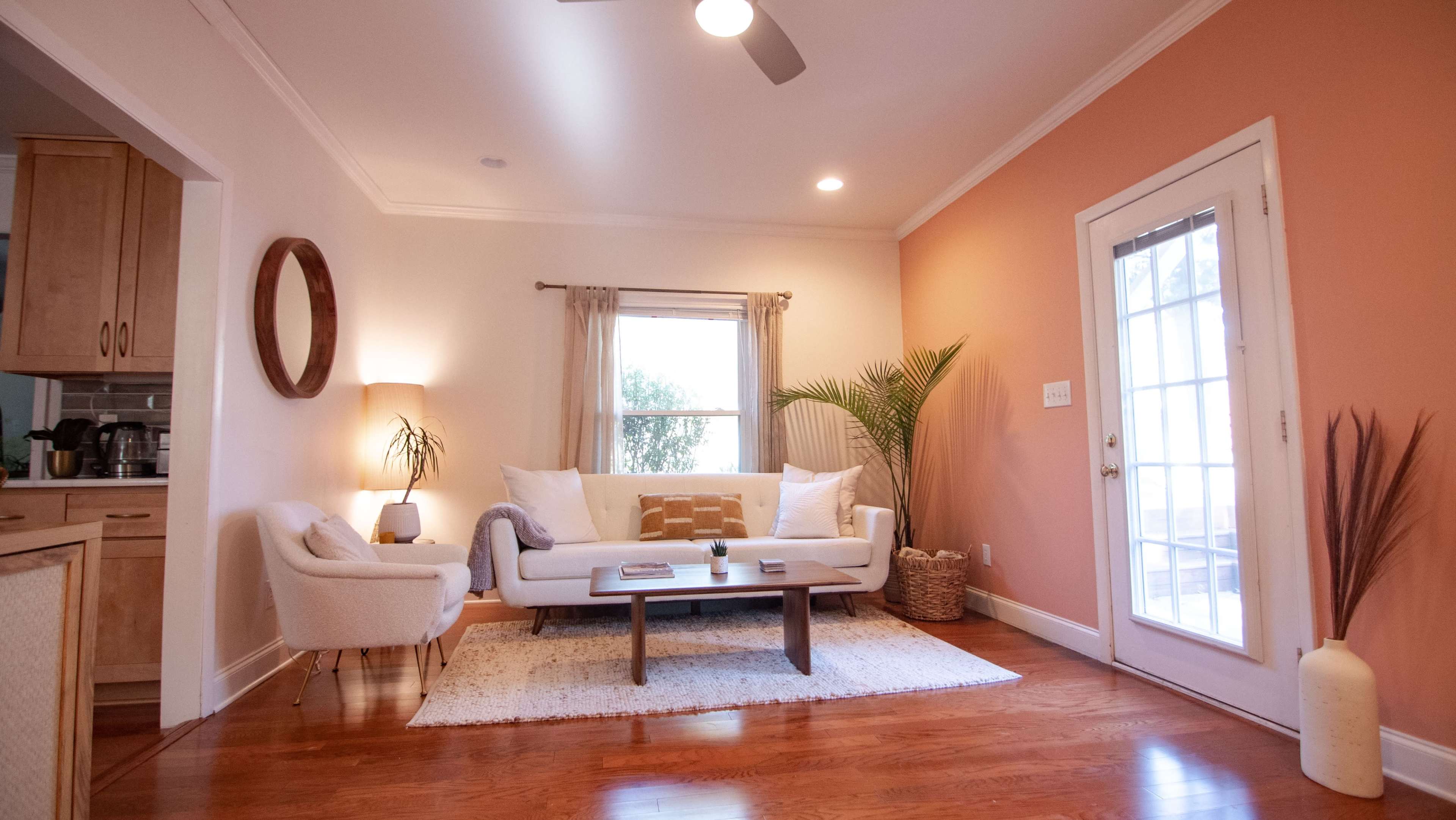 A modern living room features a white sofa, a coffee table, and large windows with natural light.