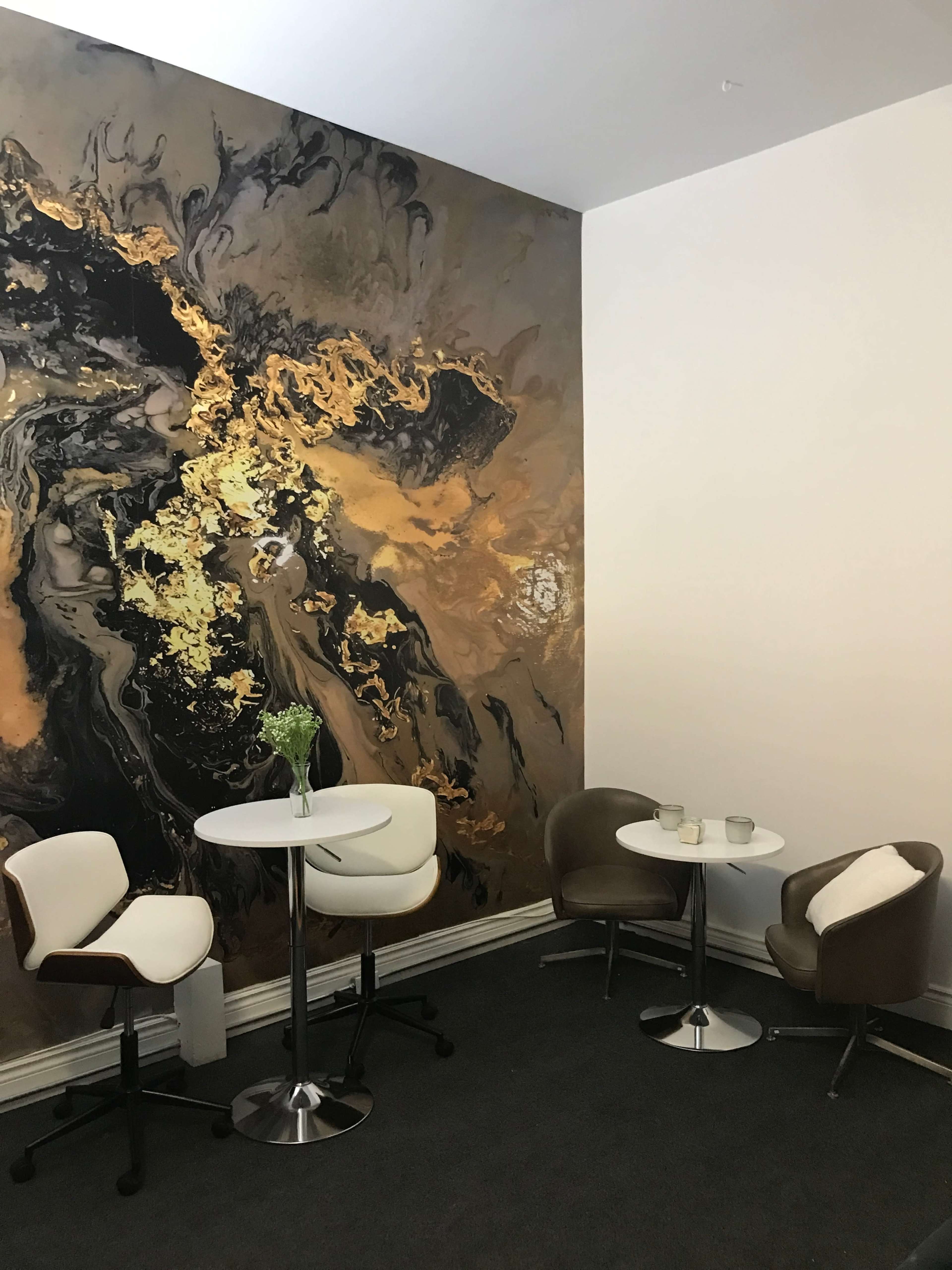 A small seating area featuring two tables and three chairs, set against a wall with an abstract gold and black mural.