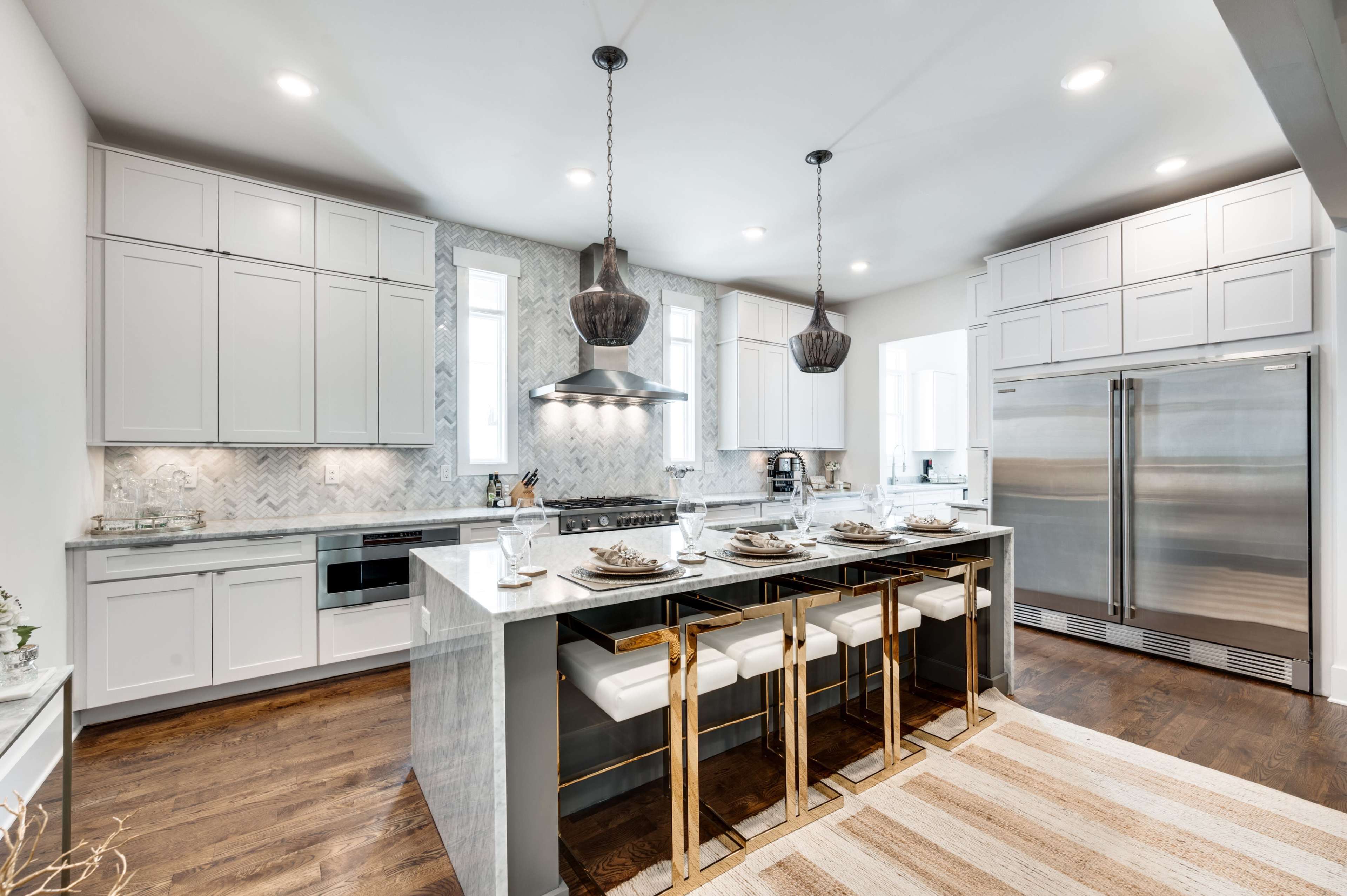 The image shows a modern kitchen featuring white cabinetry, stainless steel appliances, a large island with gold accents, and pendant lighting.