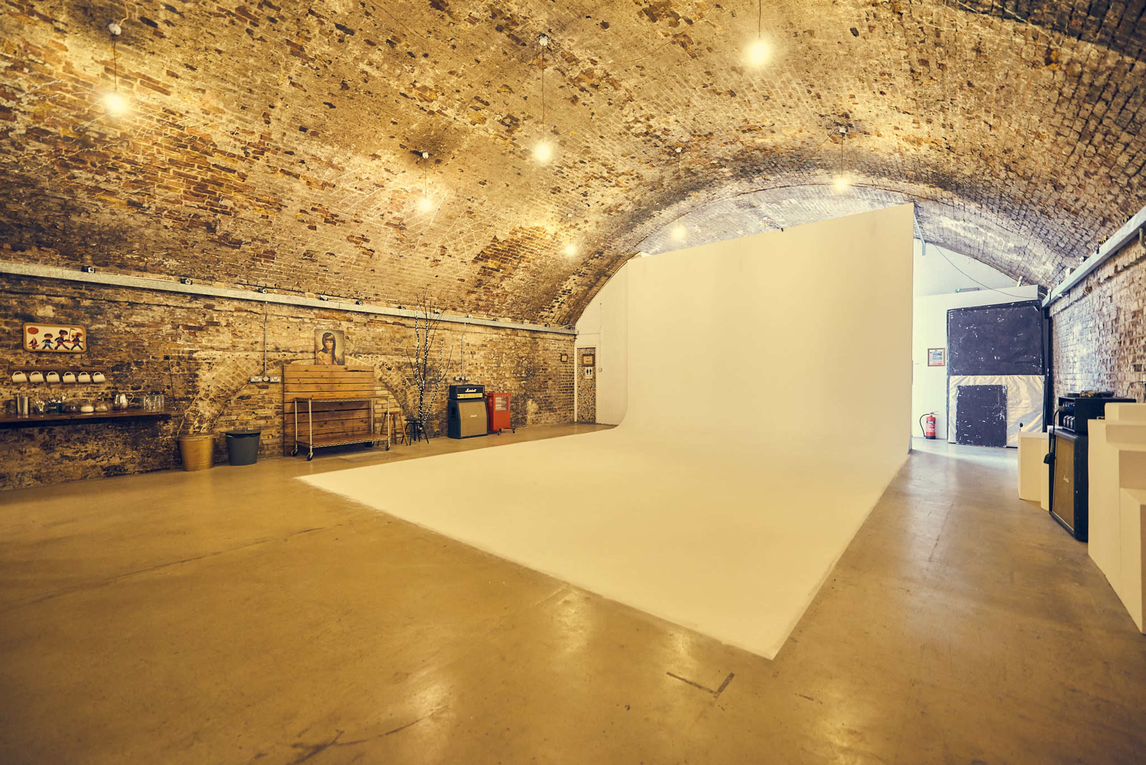 A spacious photography studio with a white backdrop, exposed brick walls, and concrete flooring.